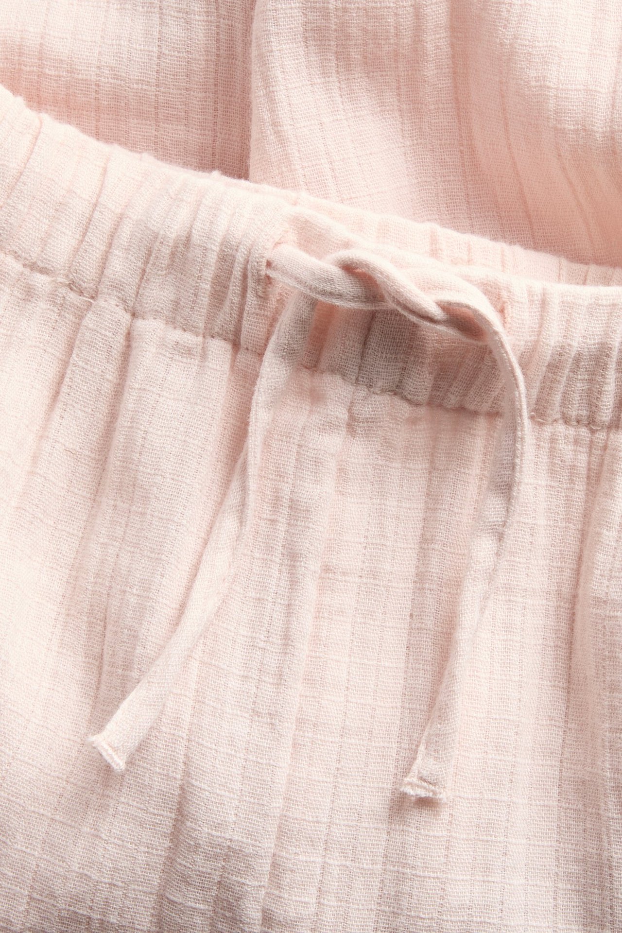 Close-up of light pink woven cotton trousers with an elasticated waist and functional drawstring.