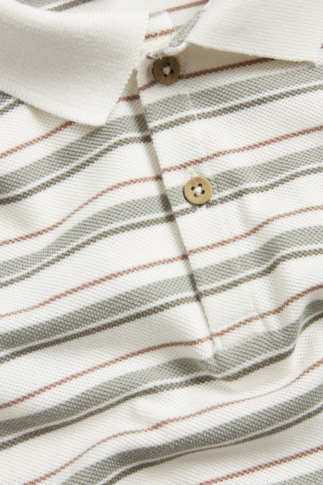 Close-up of a cream striped pique polo shirt with gray-green and brown stripes, with wooden buttons.