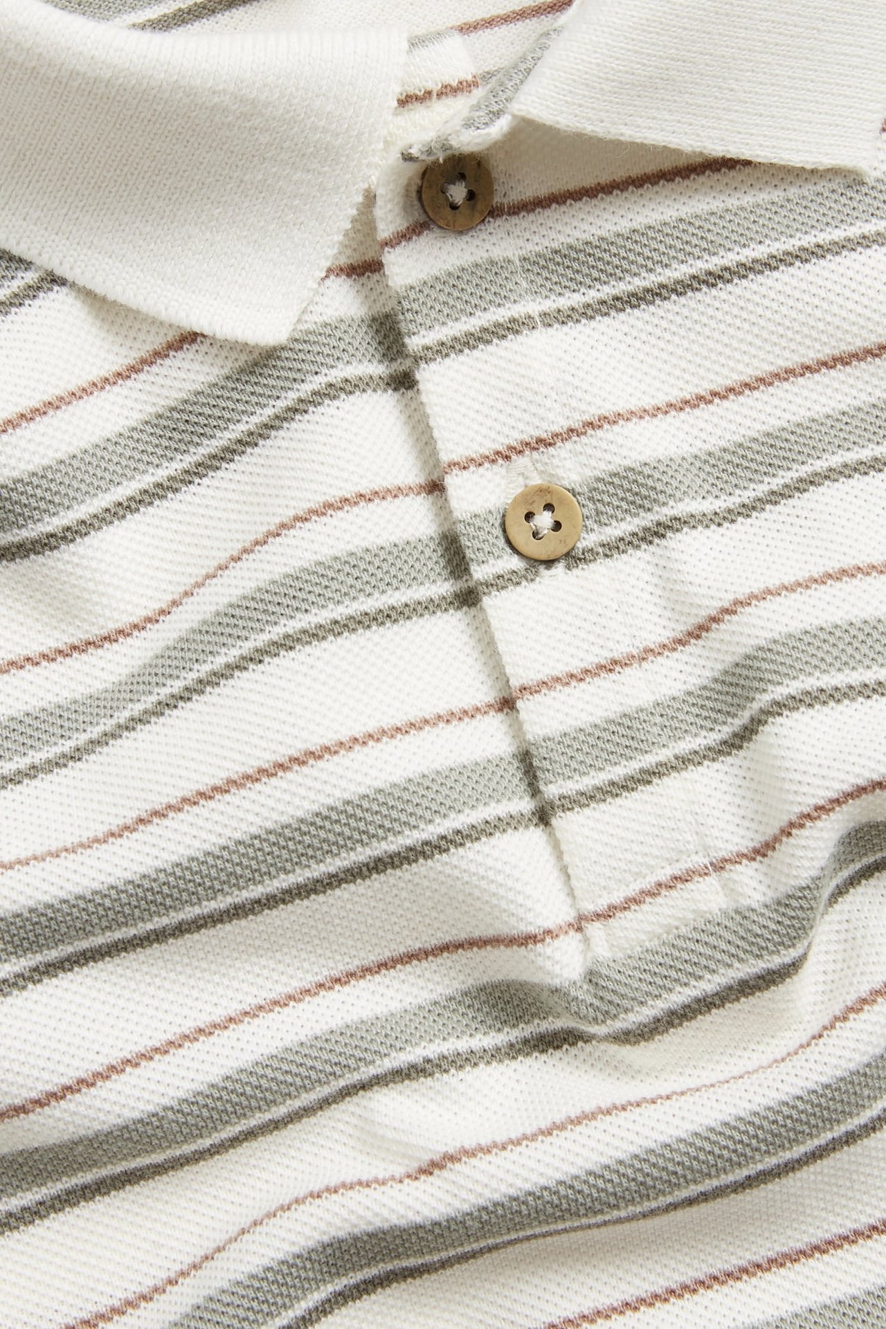 Nahaufnahme: cremefarbenes, gestreiftes Piqué-Poloshirt mit grau-grünen und braunen Streifen, Holzknöpfen.