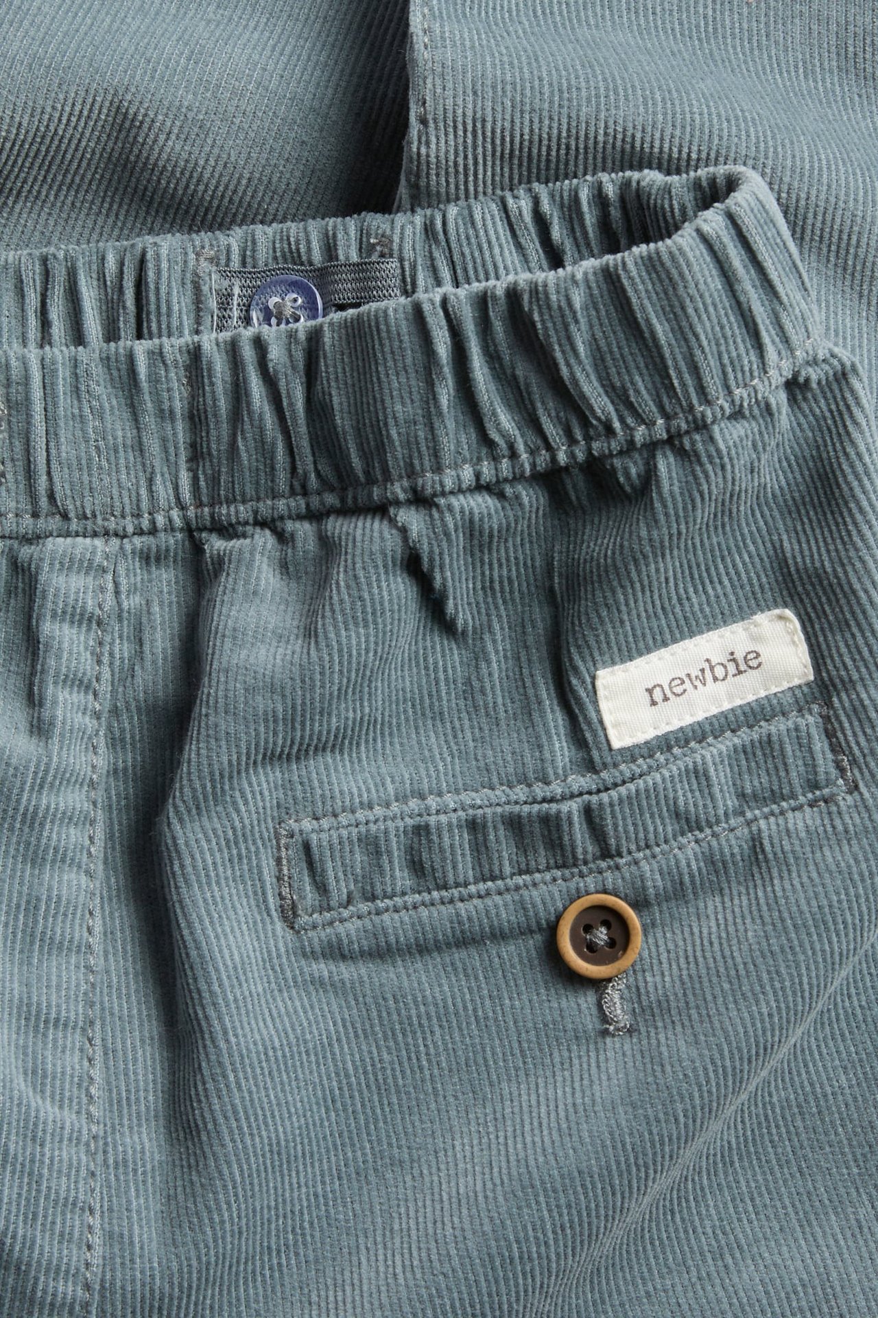 Nahaufnahme einer blauen Baby-Cordhose mit Gummizugbund und einer Gesäßtasche mit Knopf.