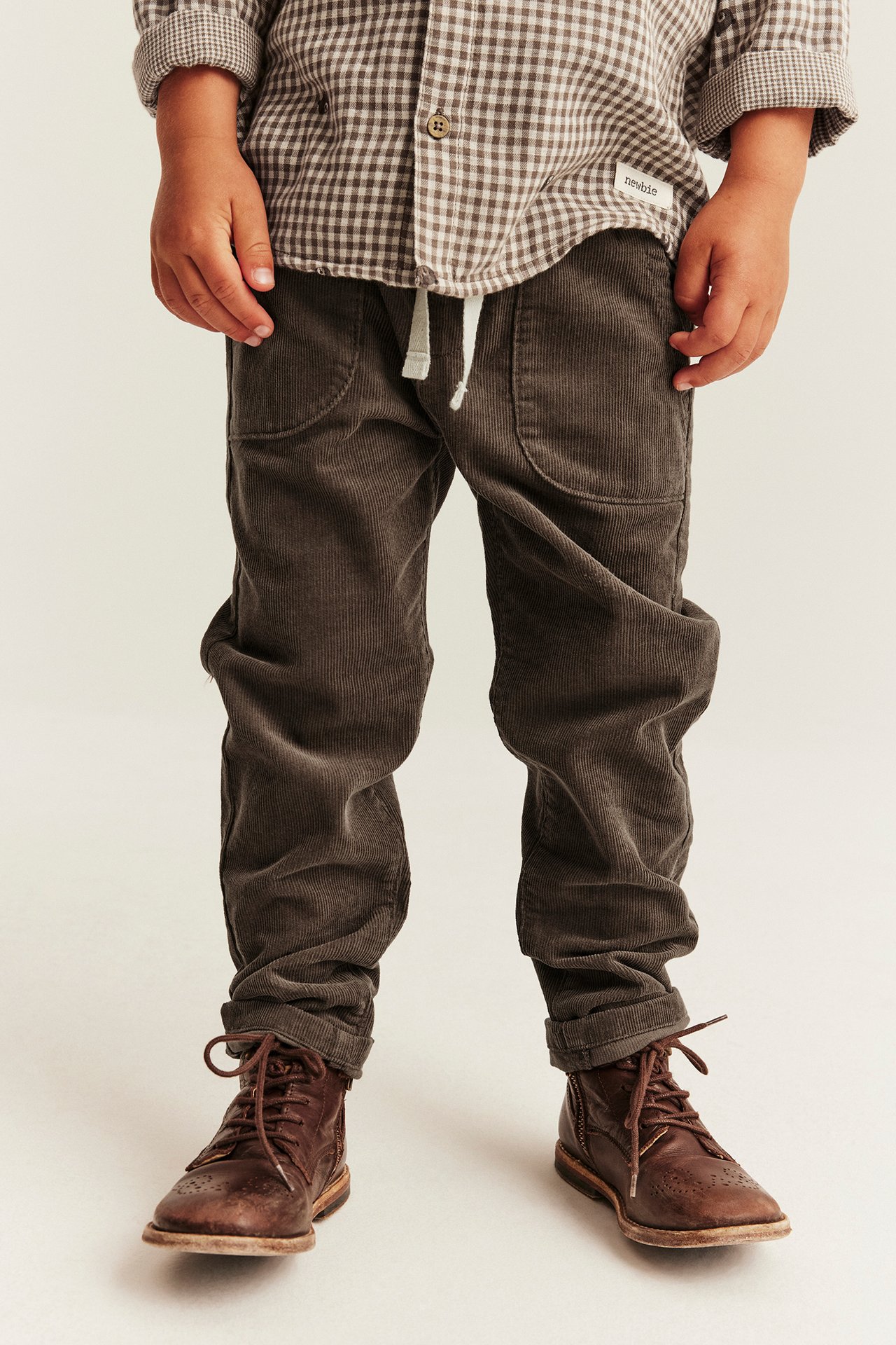 Front view: Kid in brown corduroy pants, brown checkered shirt, and brown lace-up boots.