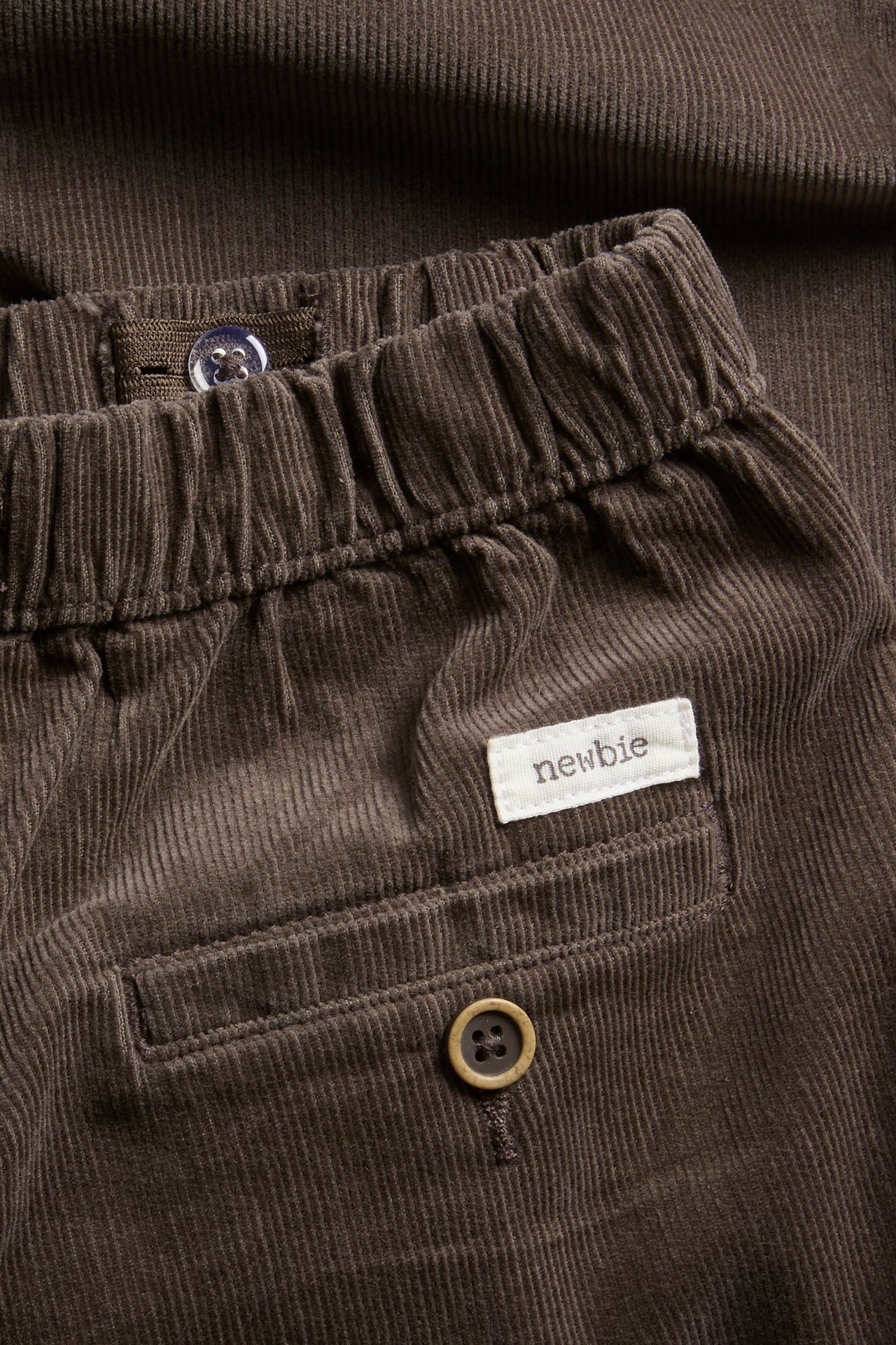 Nahaufnahme einer braunen Baby-Cordhose mit elastischem Bund und dekorativem Knopf an der Gesäßtasche.