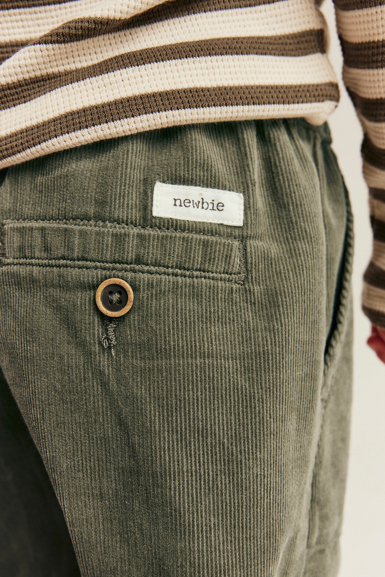 Nahaufnahme von Kinder-Cordhose in Oliv mit Knopf-Gesäßtasche und gestreiftem Oberteil.