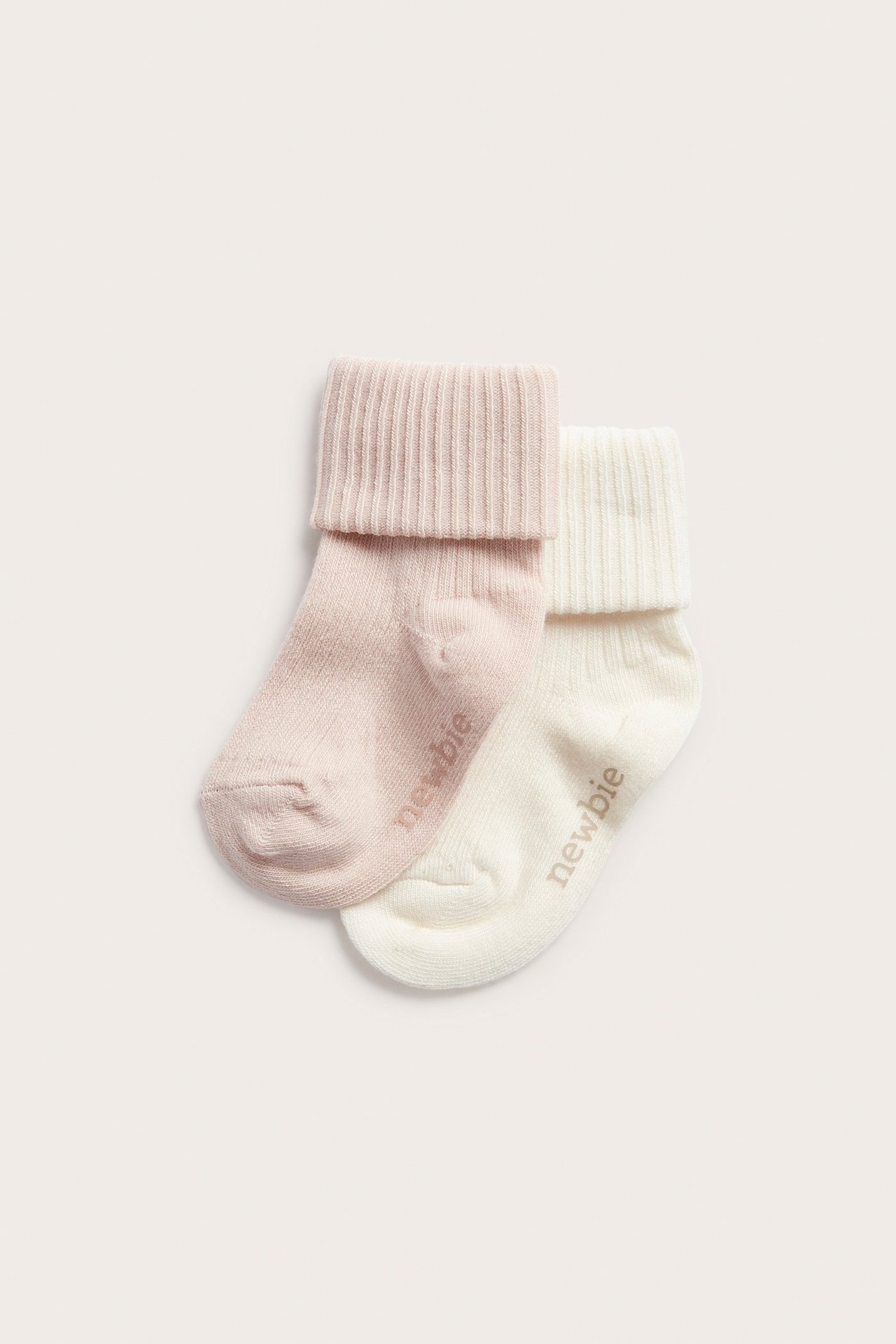 Vorderansicht, ein Zweierpack weiche, gerippte Babysocken: hellrosa und cremeweiß mit umgeschlagenen Bündchen.