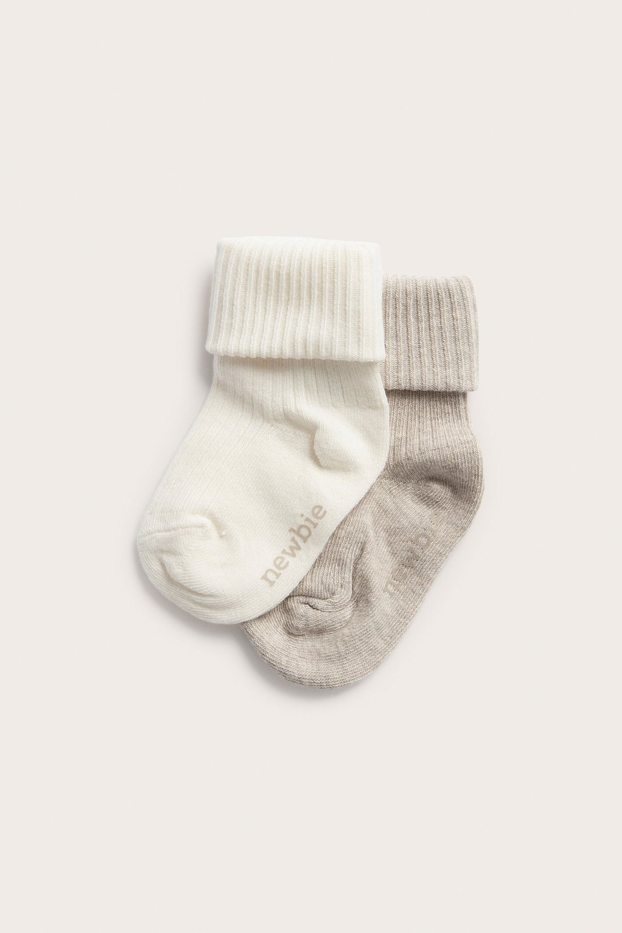 Draufsicht auf zwei Paar gerippte Babysocken: eine cremeweiße und eine beige Melange, beide mit umgeschlagenem Bündchen.