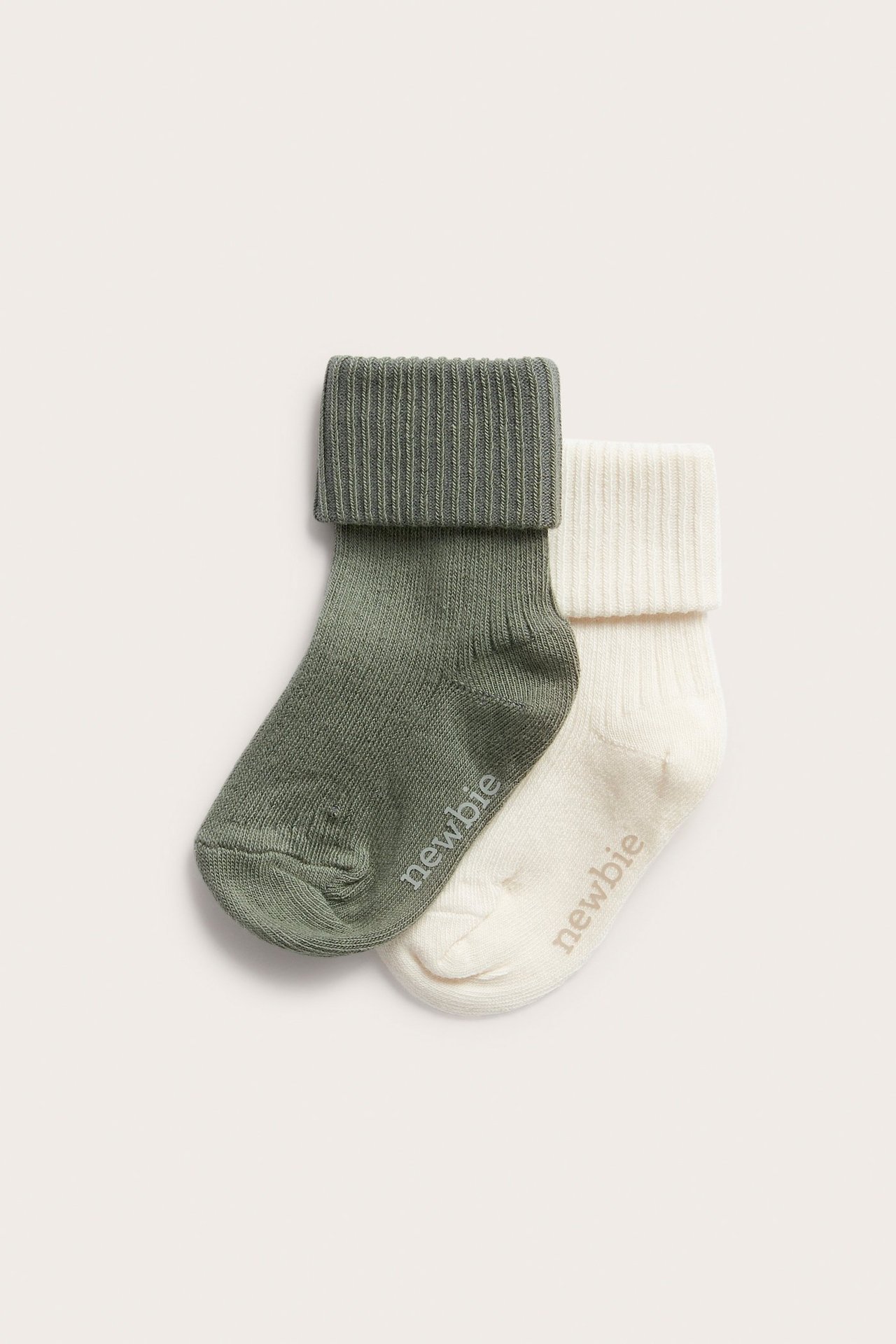 Zwei gerippte Babysocken, dunkelgrün und cremeweiß, mit umgeschlagenen Bündchen und Newbie-Logo.