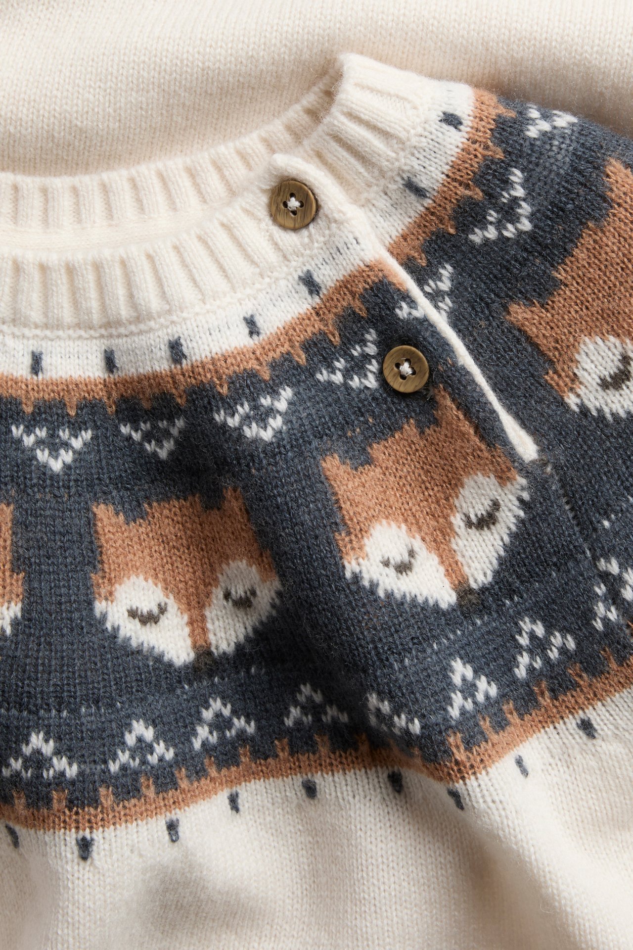 Nahaufnahme einer Baby-Cardigan in Creme, Braun und Anthrazit mit Fair Isle Fuchsmuster und Holzknöpfen.