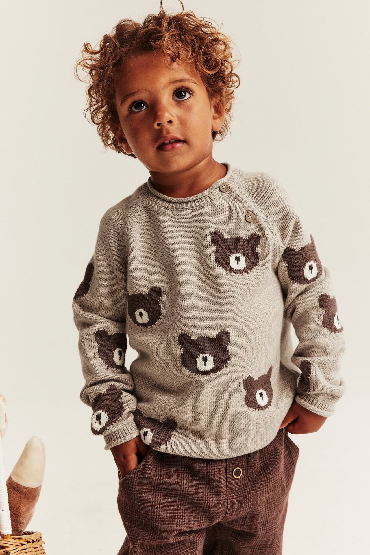 Vorderansicht eines Kindes in beigem Strickpullover mit Bären und karierter Hose.