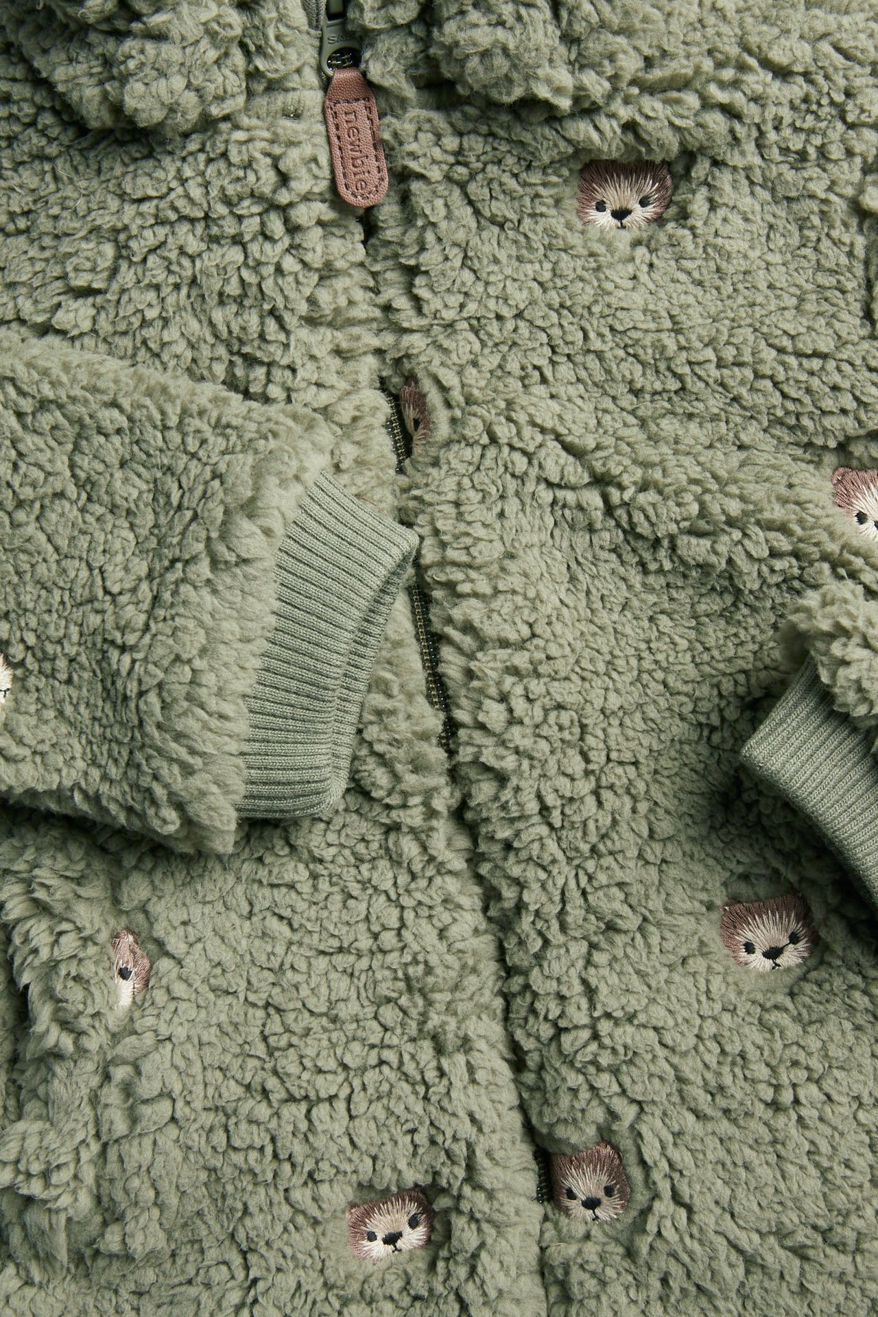 Nahaufnahme einer grünen flauschigen Babyjacke mit Igelstickereien, Reißverschluss und gerippten Bündchen.