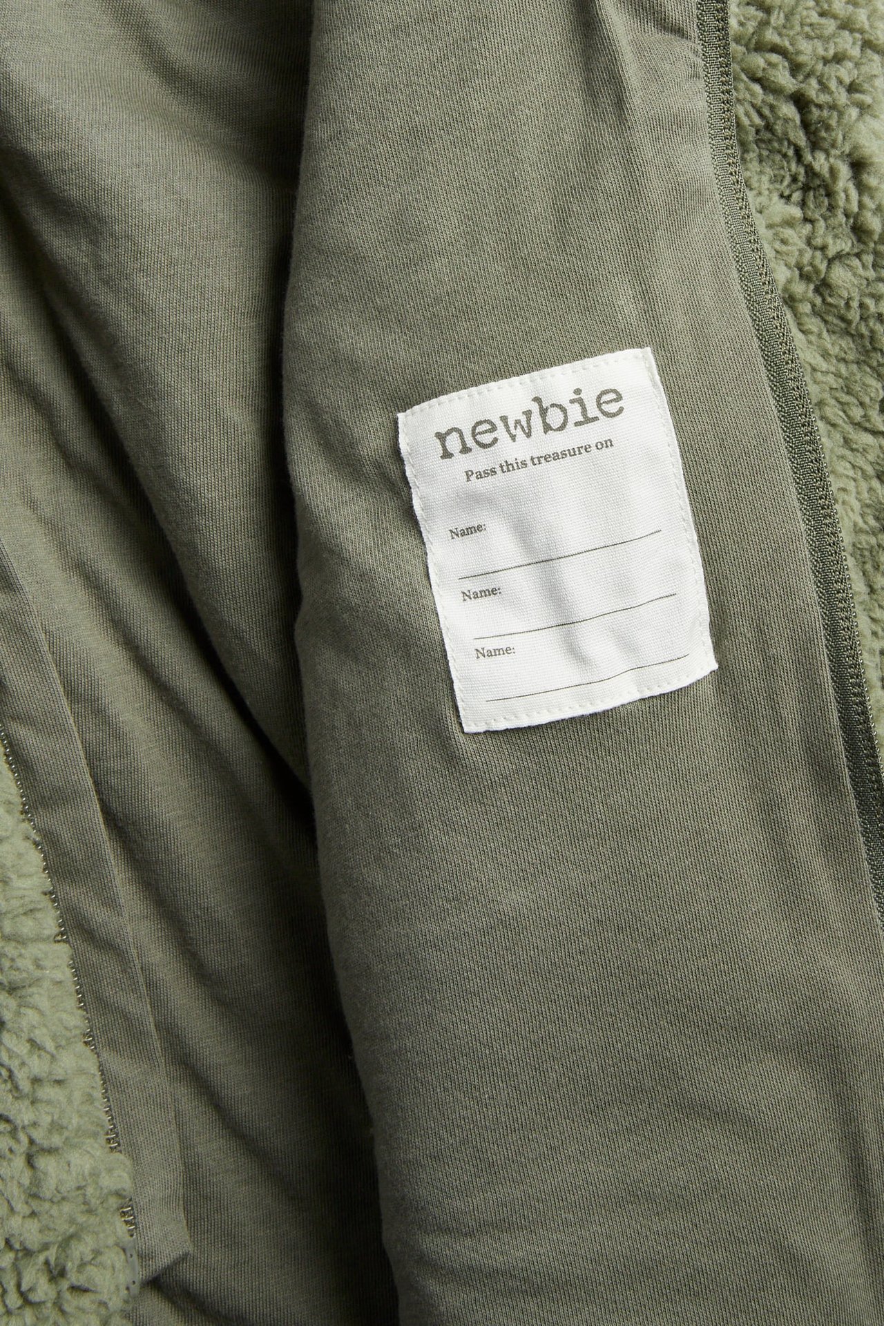 Nahaufnahme der Innenseite einer grünen flauschigen Jacke mit einem weißen 'newbie' Namensschild.