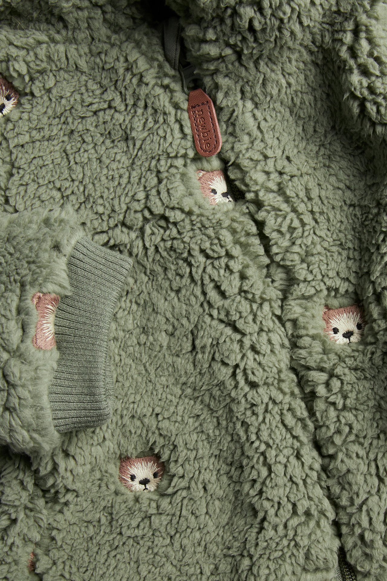 Nahaufnahme, Vorderansicht: Baby-Fleecejacke in Dunkelgrün mit Allover-Teddybärenstickerei, Reißverschluss und Rippbündchen.