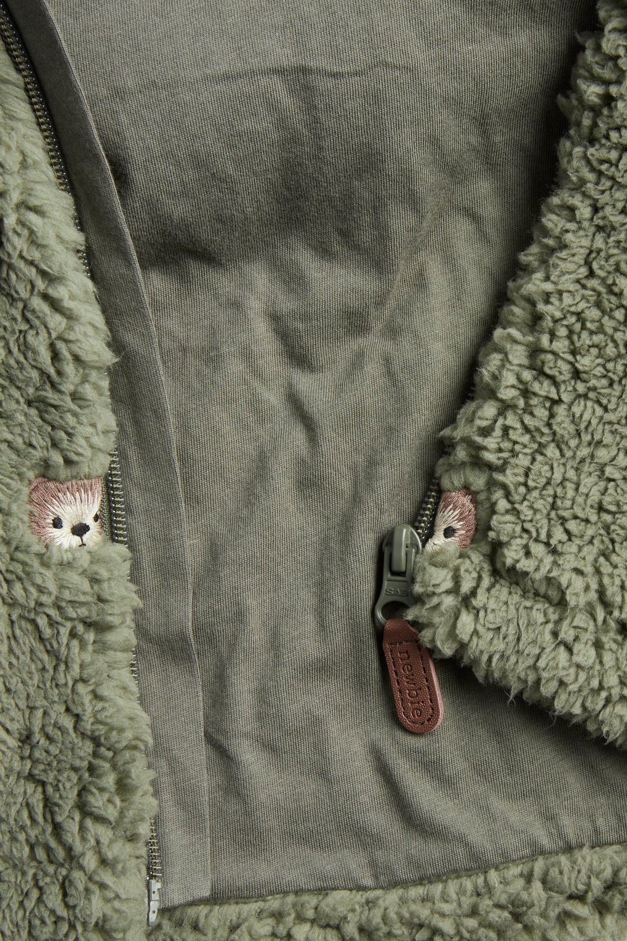 Nahaufnahme einer grünen Teddyjacke mit Reißverschluss und gestickten Bärengesichtern.