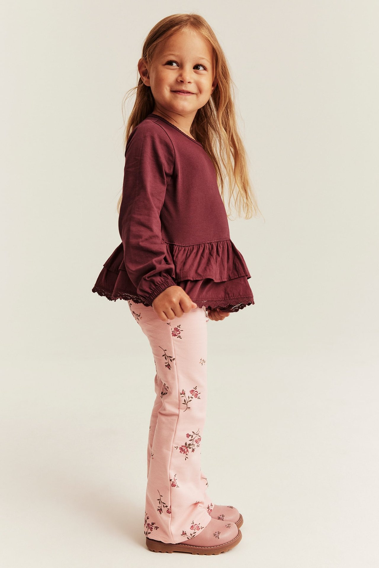 Side view of kid in burgundy ruffled top with lace hem and pink floral flared pants.