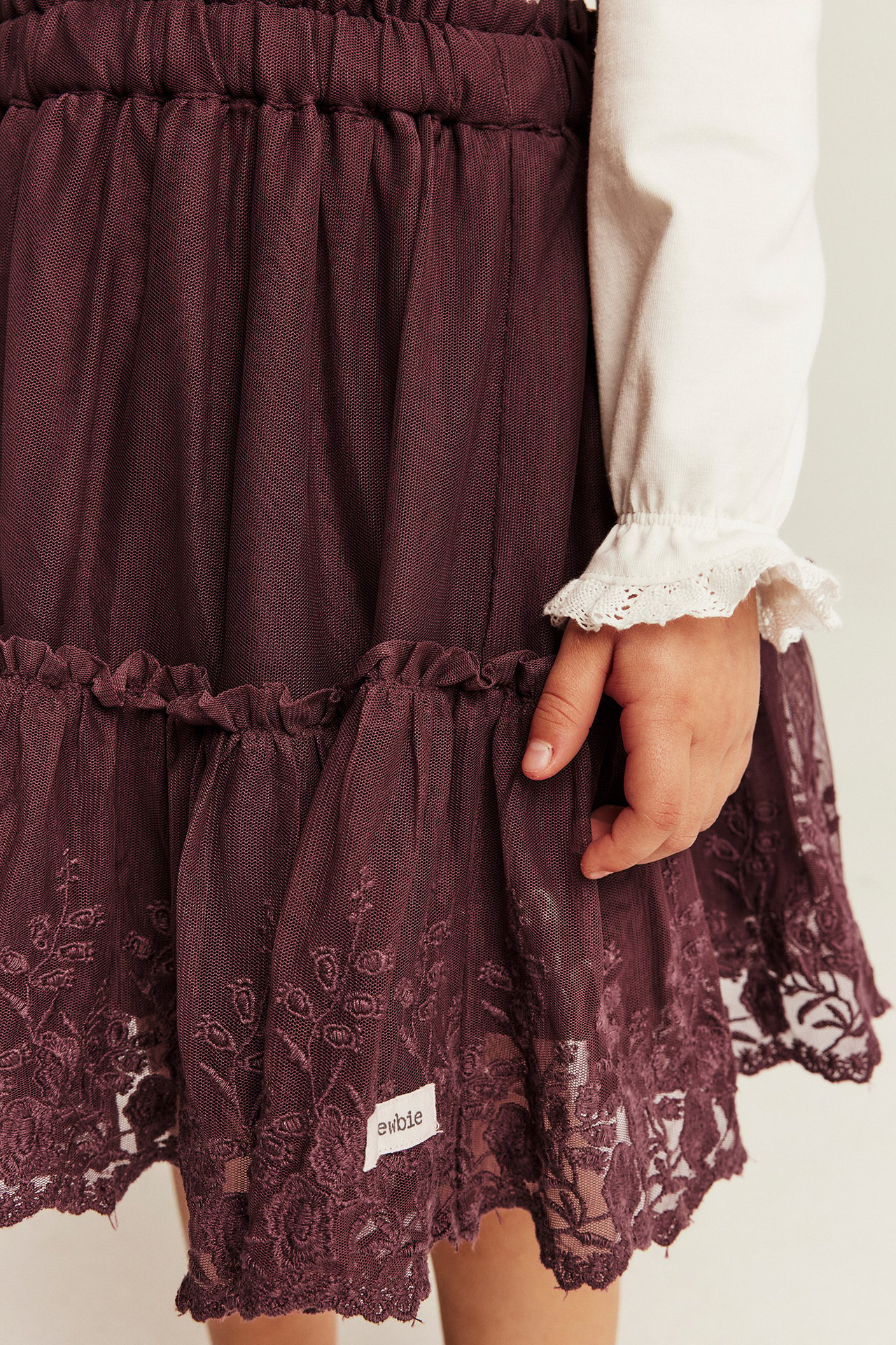 Close-up of a kid wearing a dark purple tulle skirt with lace trim and a cream long-sleeve top.