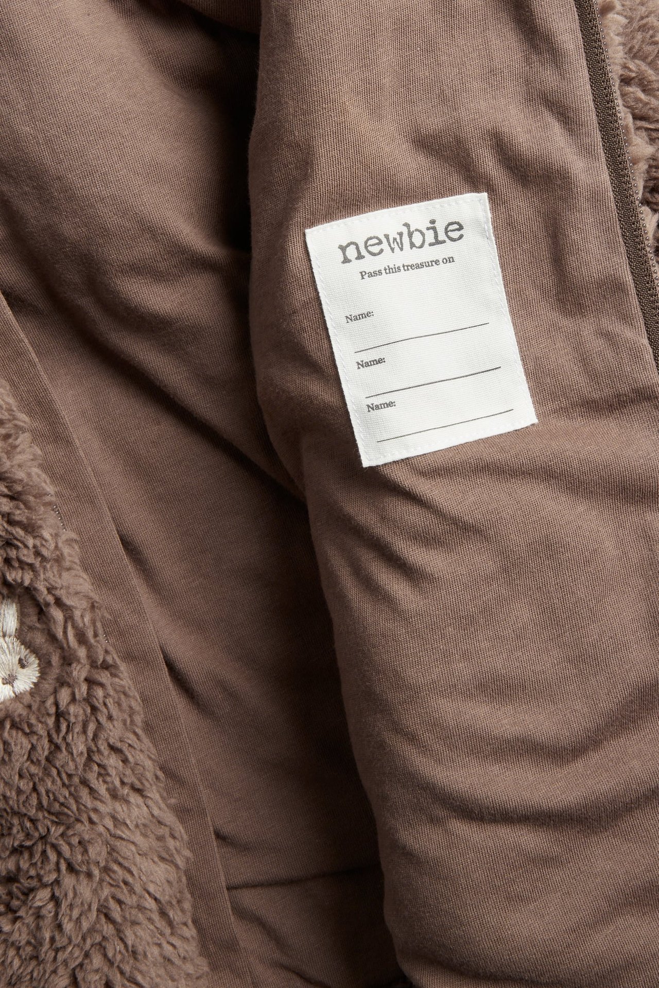 Nahaufnahme einer braunen Teddyfleece-Kleidungsinnenseite mit weißem 'Newbie'-Etikett.