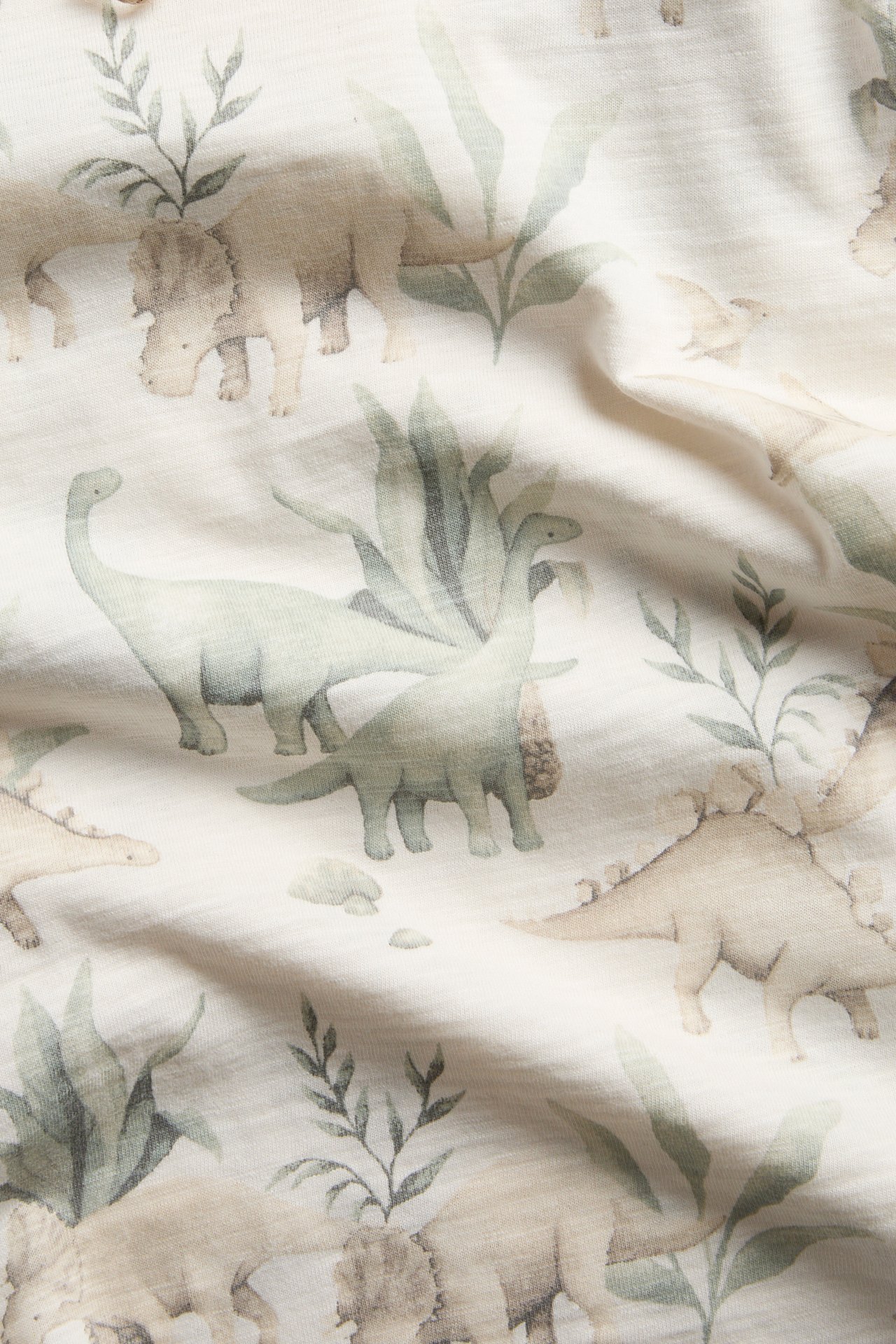 Close-up of a light fabric with a muted green dinosaur and plant print.
