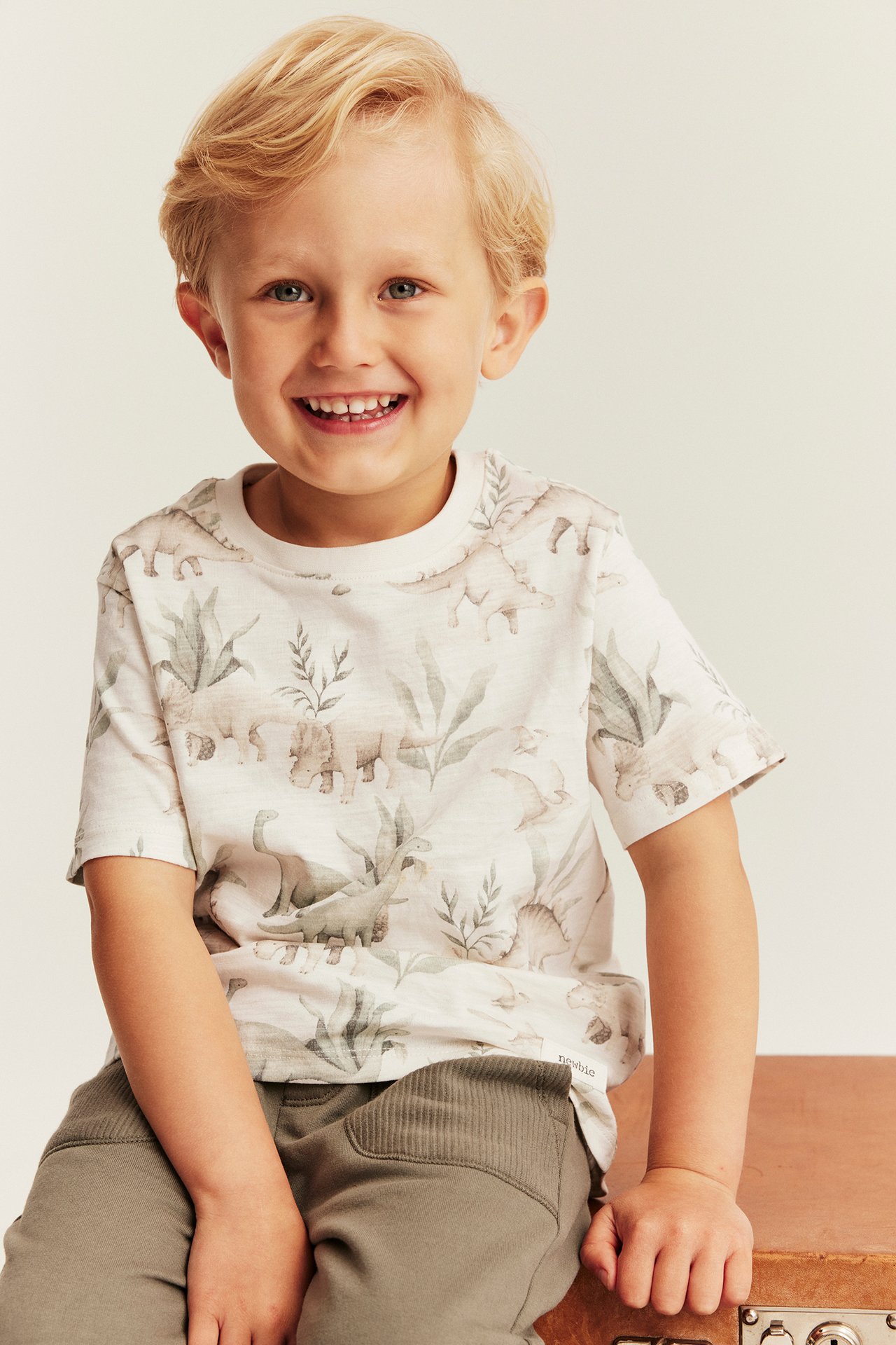 Vorderansicht eines Kindes in weißem T-Shirt mit Dinosaurier-Print und olivgrünen Jogginghosen.