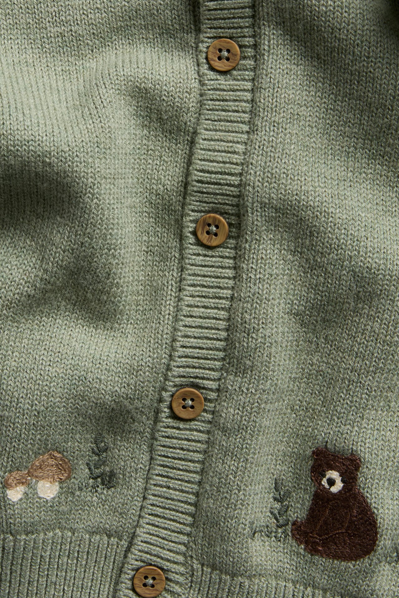 Nahaufnahme einer grünen gestrickten Kinderstrickjacke mit braunen Knöpfen und Tierstickerei.