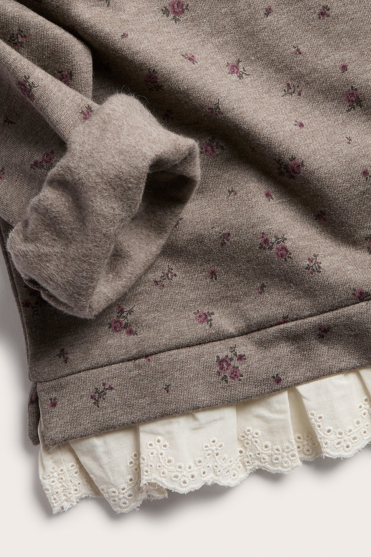 Nahaufnahme eines taupefarbenen Sweatshirts mit Blumenmuster und weißem Rüschensaum aus Spitze.