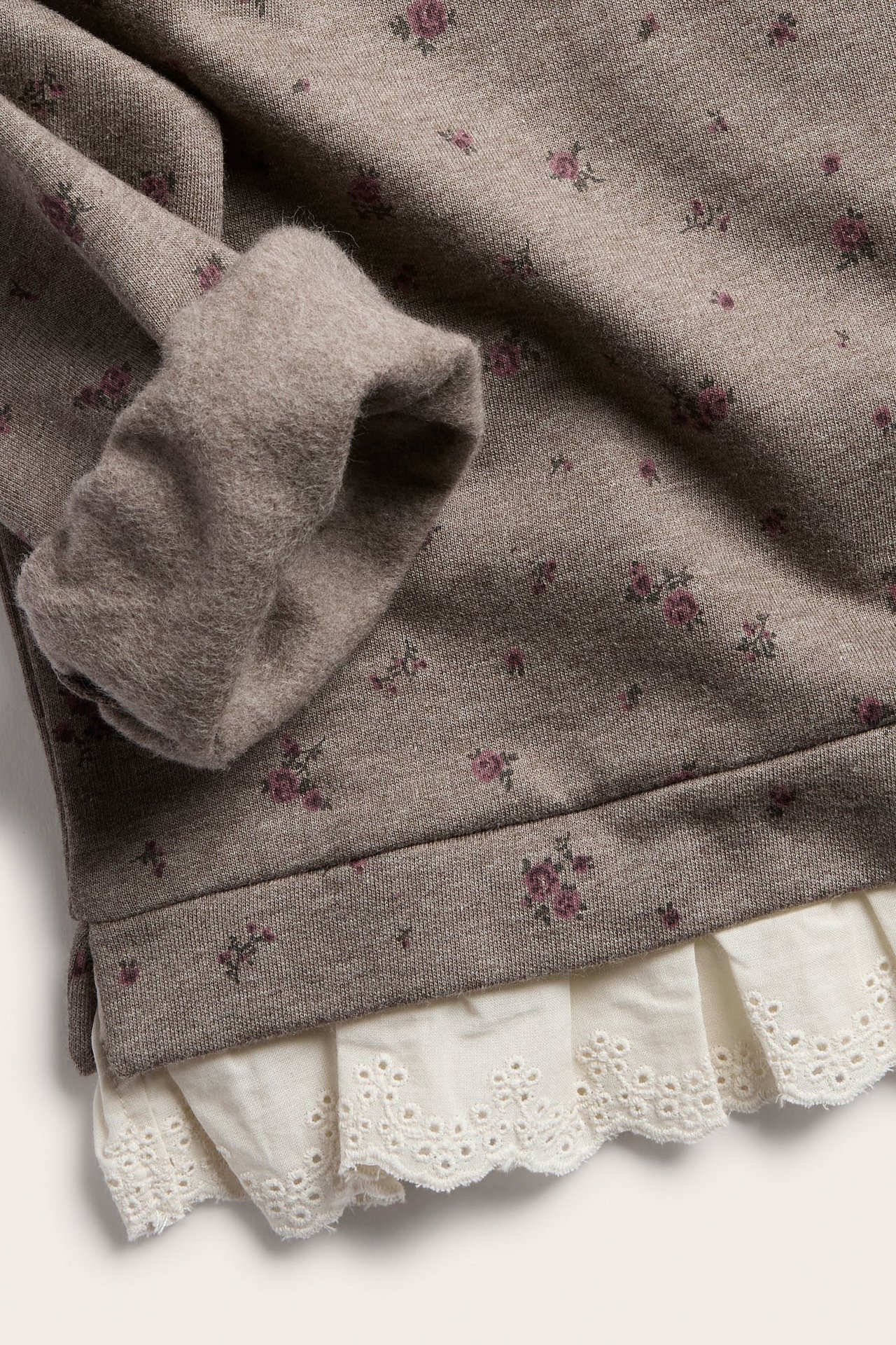 Nahaufnahme eines taupefarbenen Sweatshirts mit Blumenmuster und weißem Rüschensaum aus Spitze.