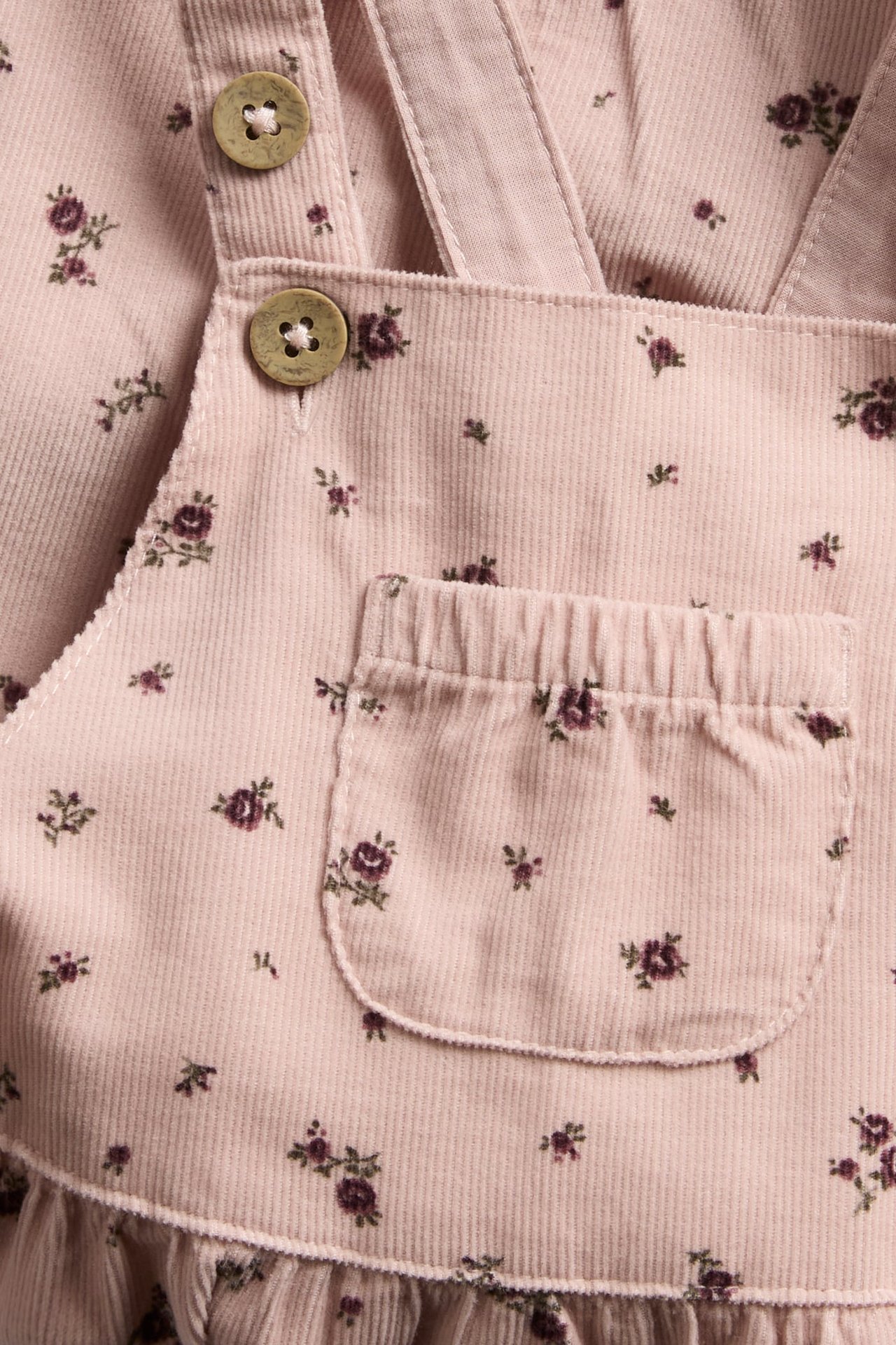 Nahaufnahme: Rosa geblümtes Cord-Overallkleid mit Knöpfen und Fronttasche.