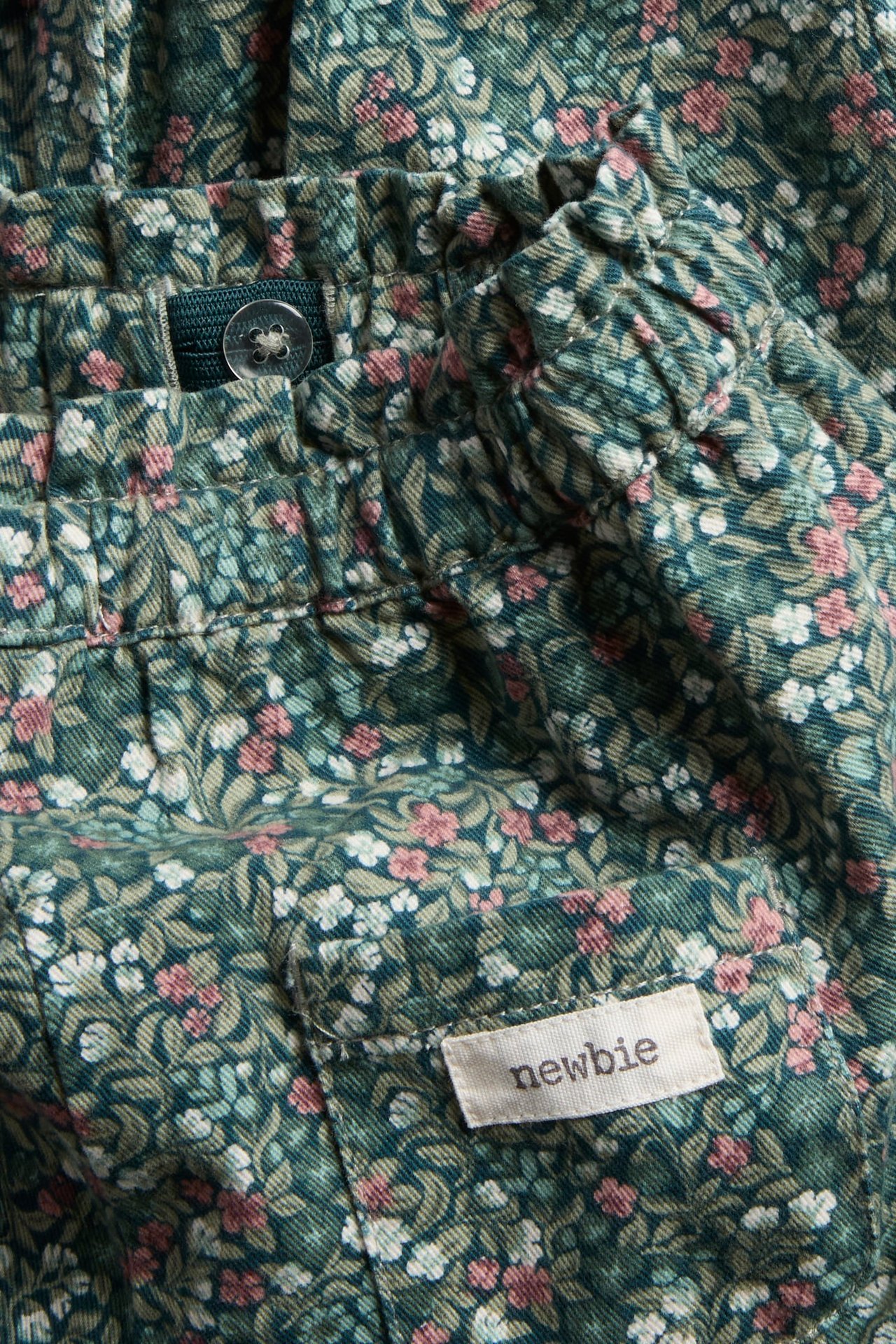 Close-up of dark green floral corduroy baby pants with an adjustable waist and a woven label.