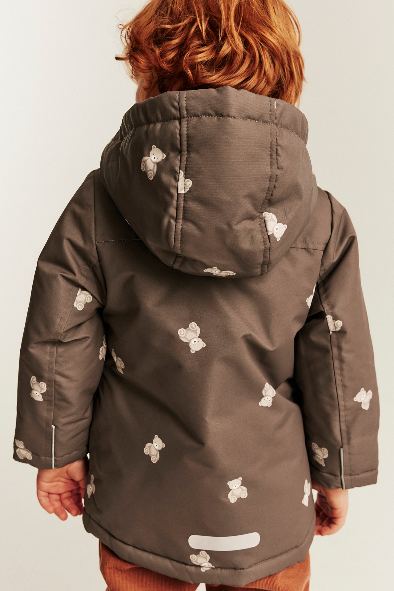 Rückansicht eines Kindes in brauner Kapuzenjacke mit Teddybär-Aufdruck.