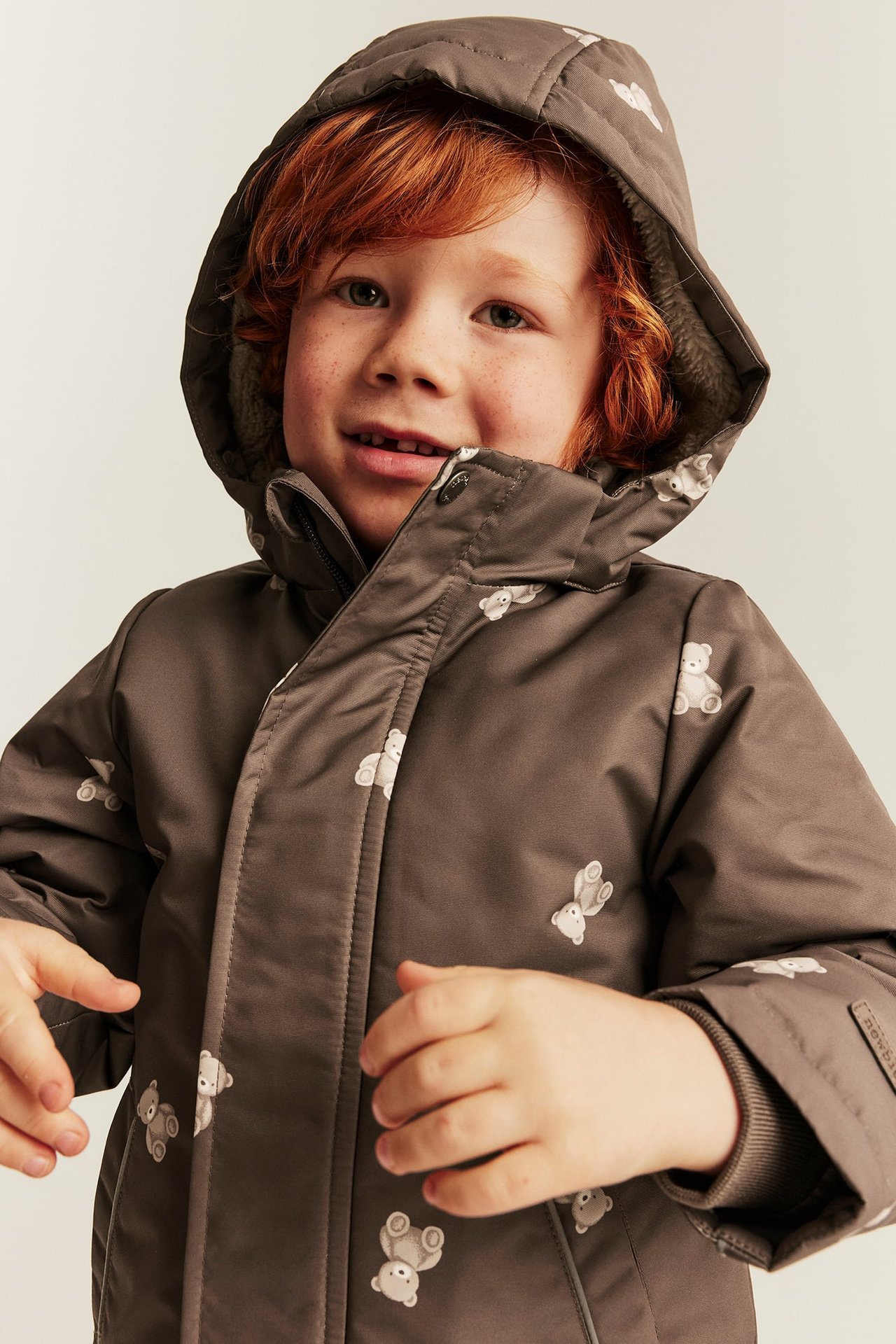 Nahaufnahme, Vorderansicht eines Kindes in brauner Kapuzenjacke mit weißem Teddybärmuster und Reißverschluss.