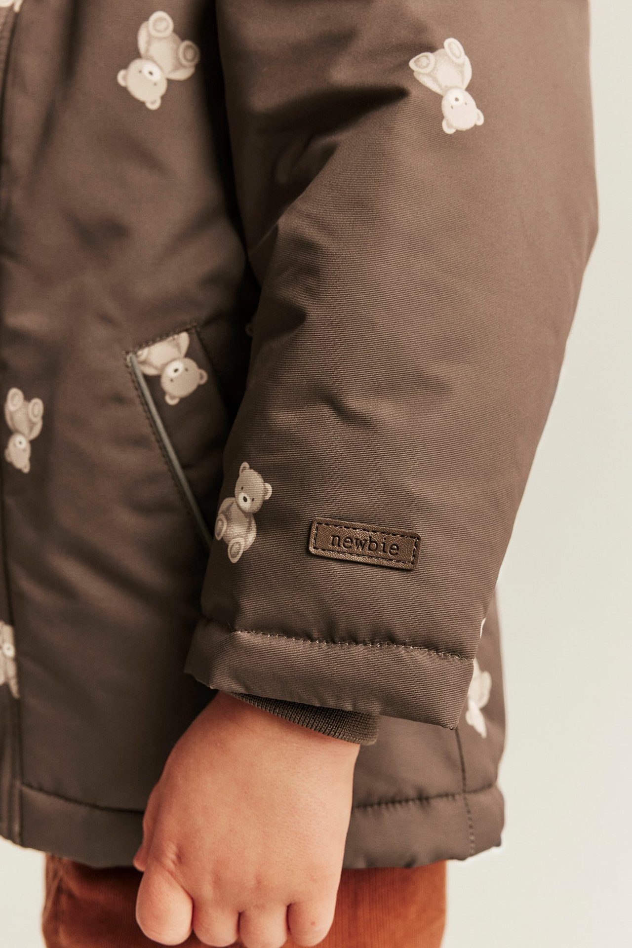 Nahaufnahme von brauner Kinder-Steppjacke mit Teddybärmuster und "newbie"-Etikett am Ärmel.