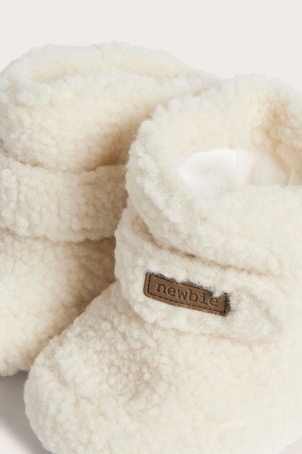 Close-up of cream fluffy baby booties with a brown 'newbie' label.