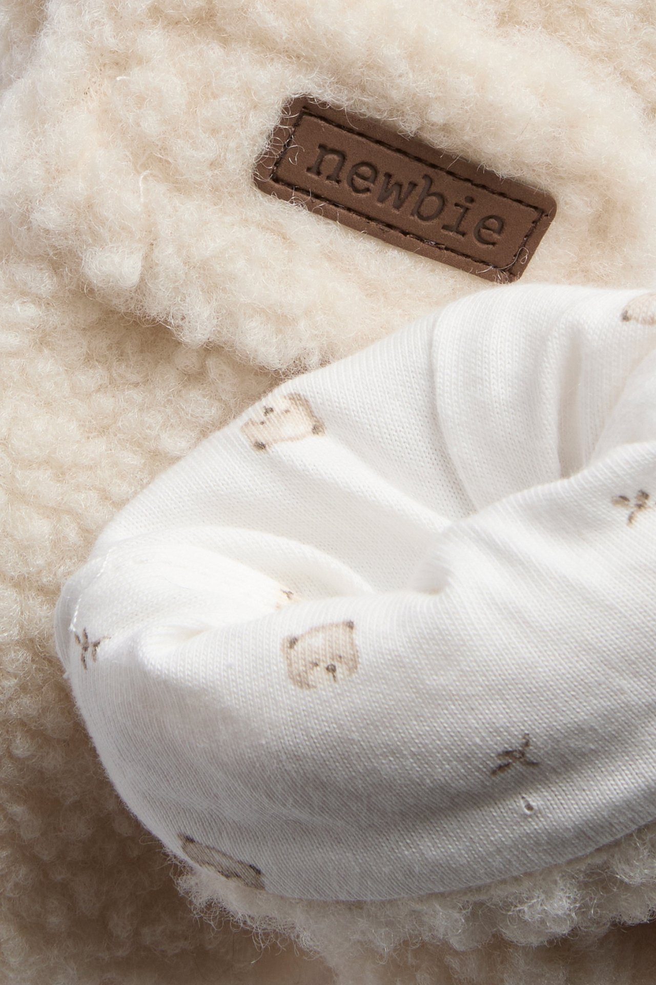 Close-up of a white baby garment with bear pattern, next to a brown label and fluffy cream fabric.