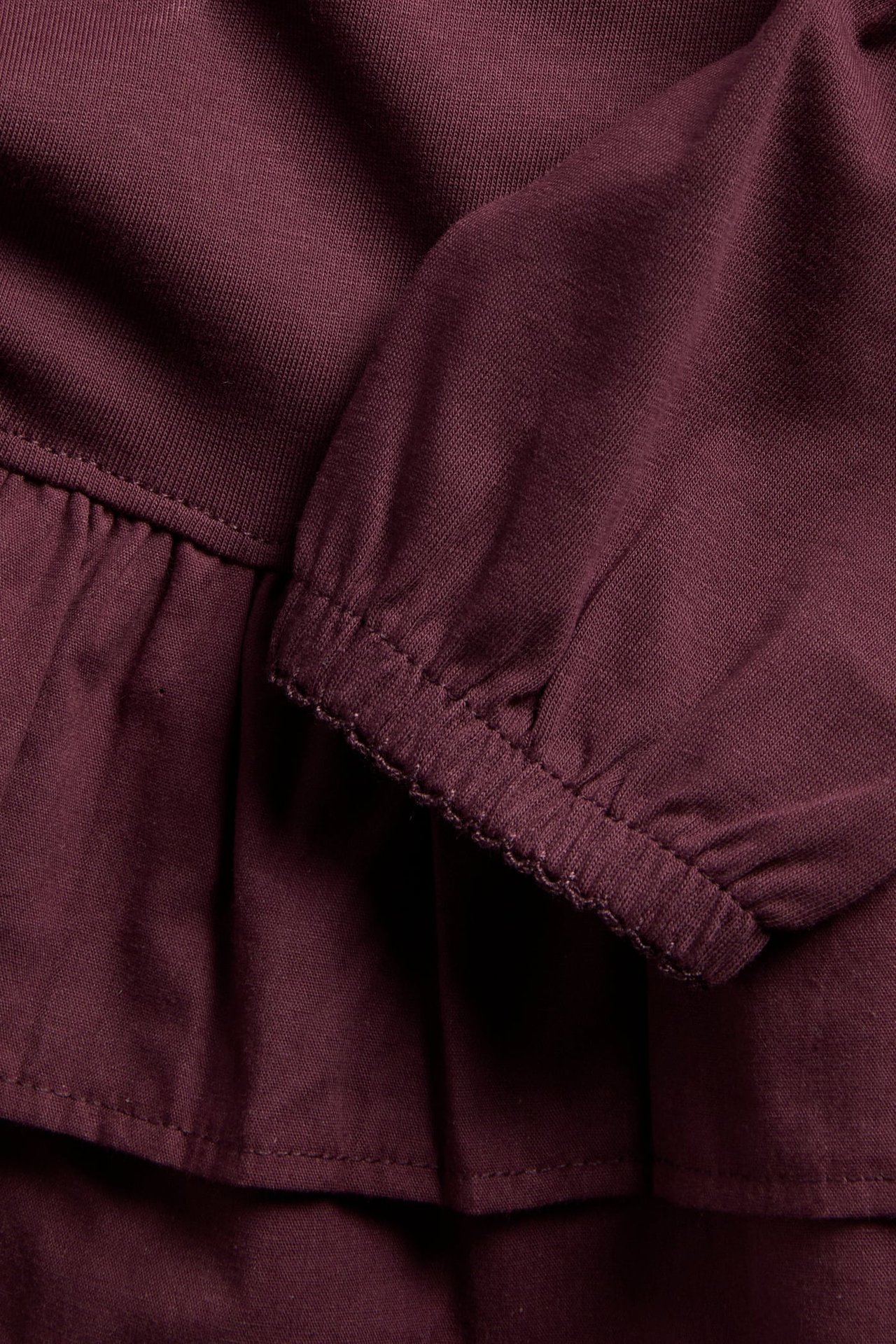 Nahaufnahme eines bordeauxroten Strickkleidungsstücks mit Rüschen und elastischem Bündchen.