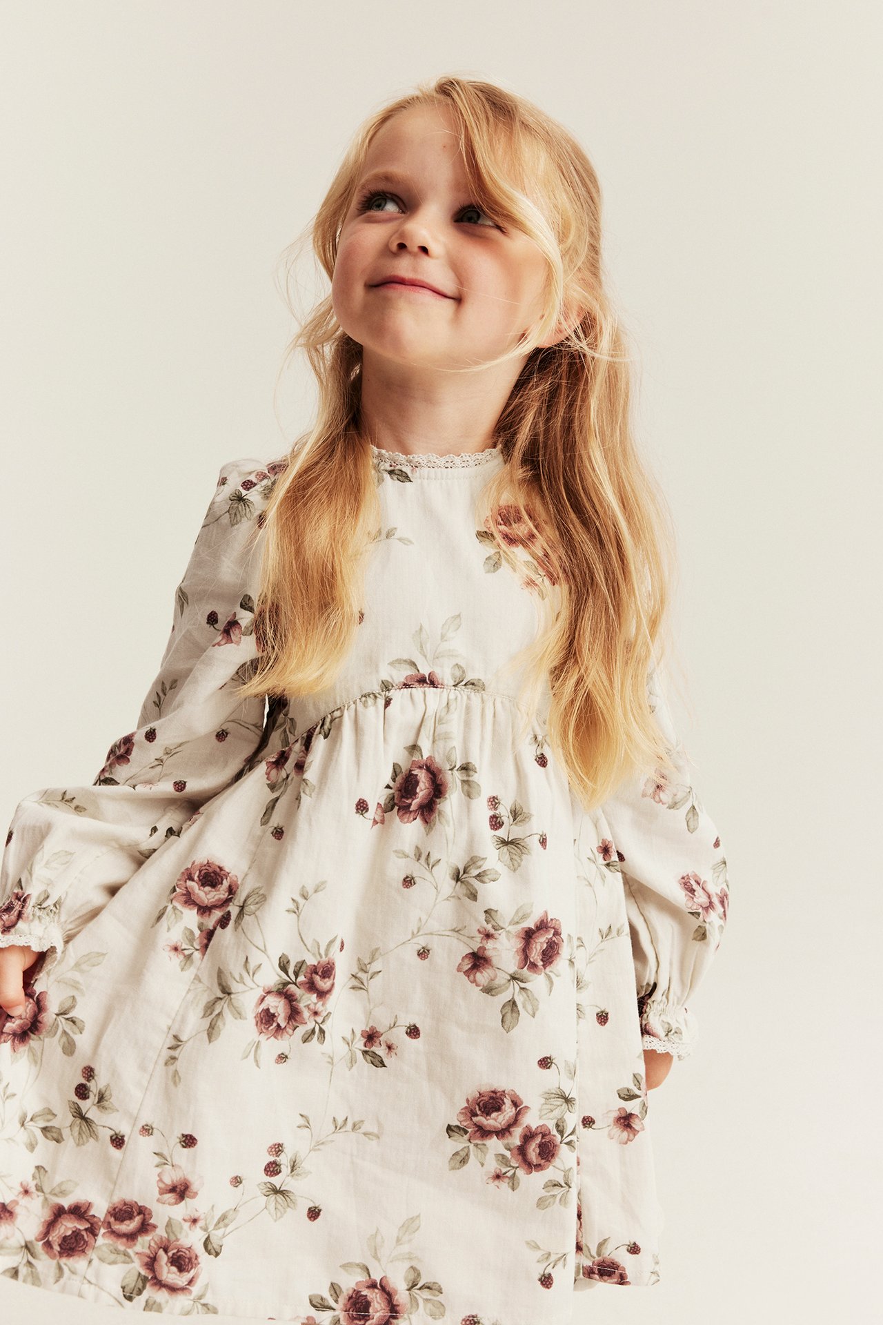 Vorderansicht eines Kindes in einem langärmeligen cremefarbenen Kleid mit dunkelrosa Rosen- und Beerenmuster.