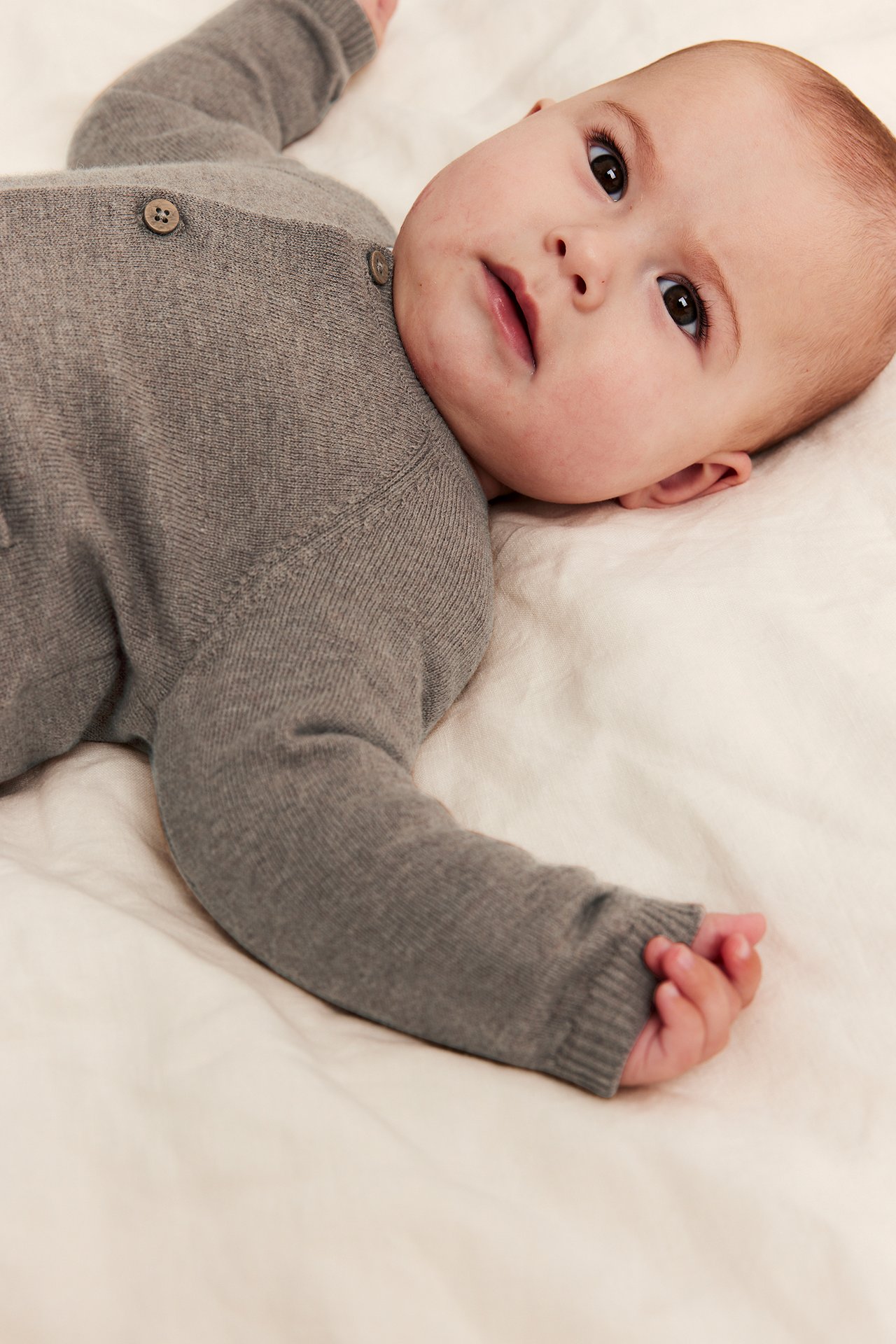 Close-up of a baby wearing a grey knitted cardigan with visible buttons on the back, lying down.