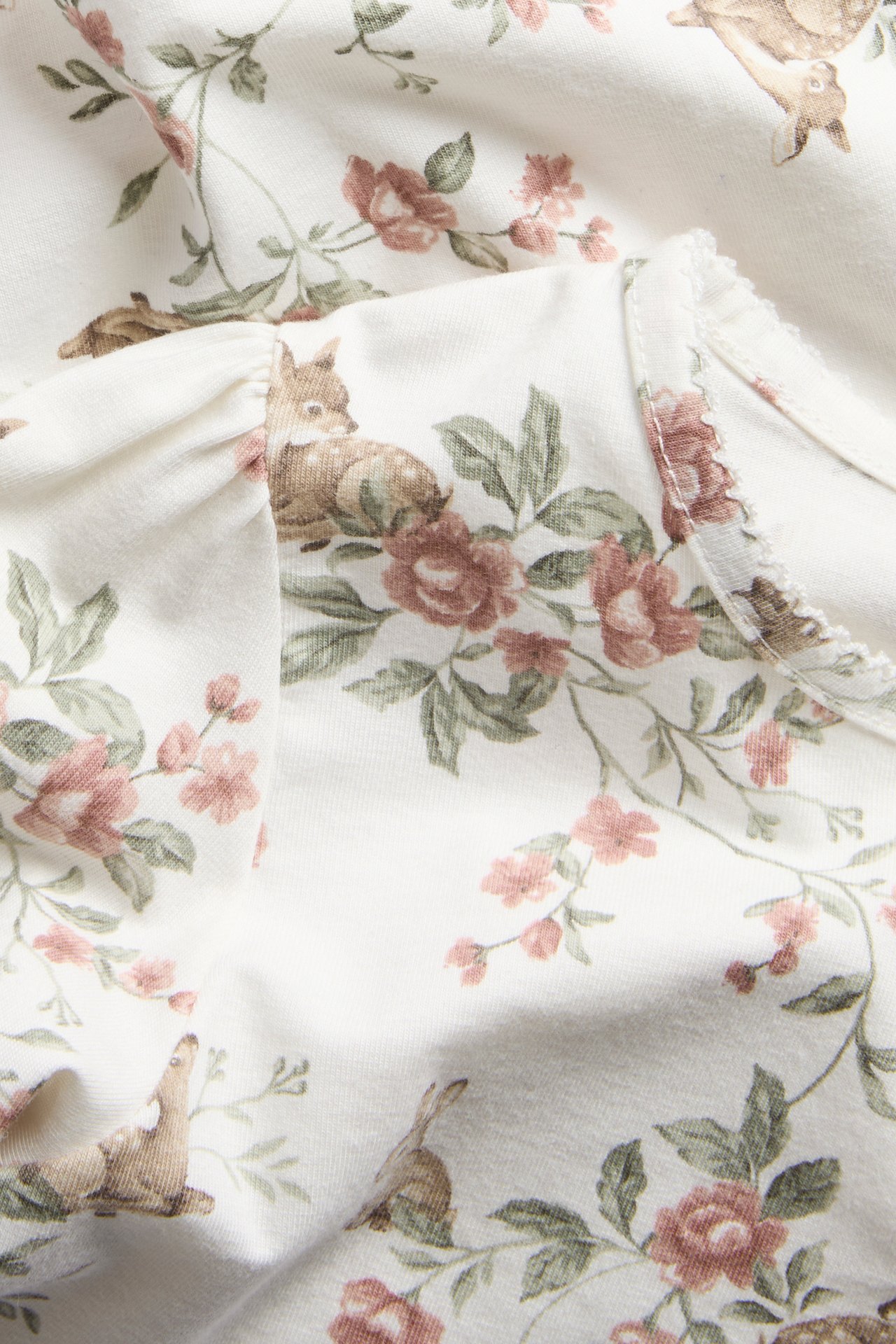 Nahaufnahme eines cremefarbenen Langarmshirts mit Reh- und Blumendruck, Gummibündchen und Picotsaum.