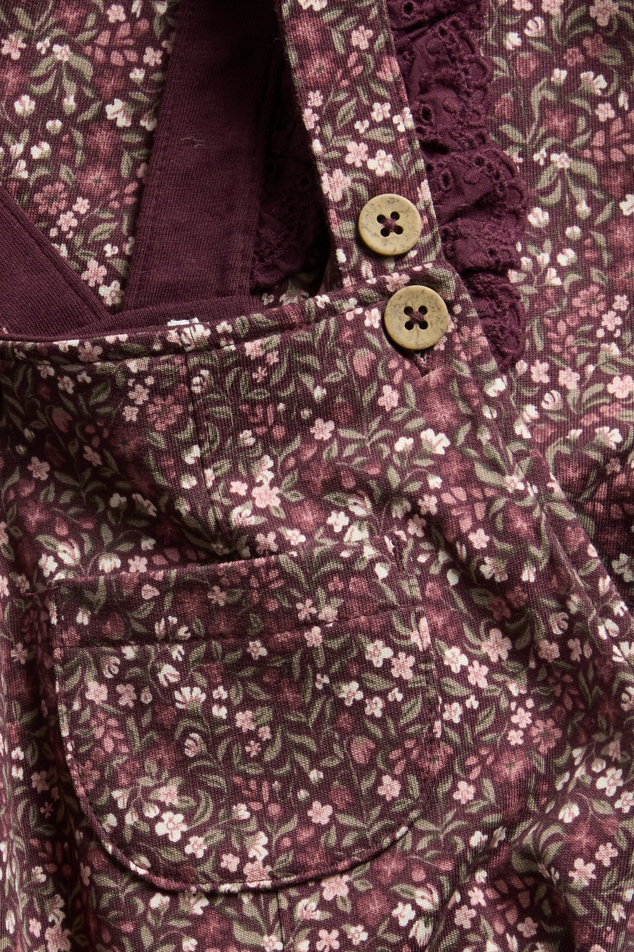 Close-up of a kid's dark floral corduroy pinafore dress, buttoned, with a lace collar.