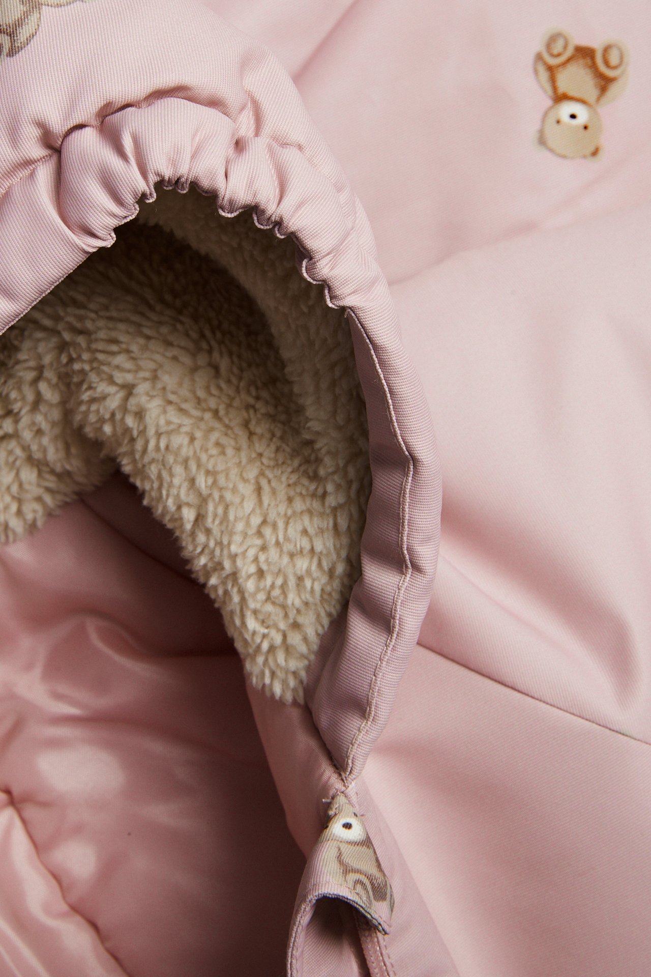 Nahaufnahme eines pinken Babyschlafsacks mit flauschigem beigem Futter und Bärendetails.