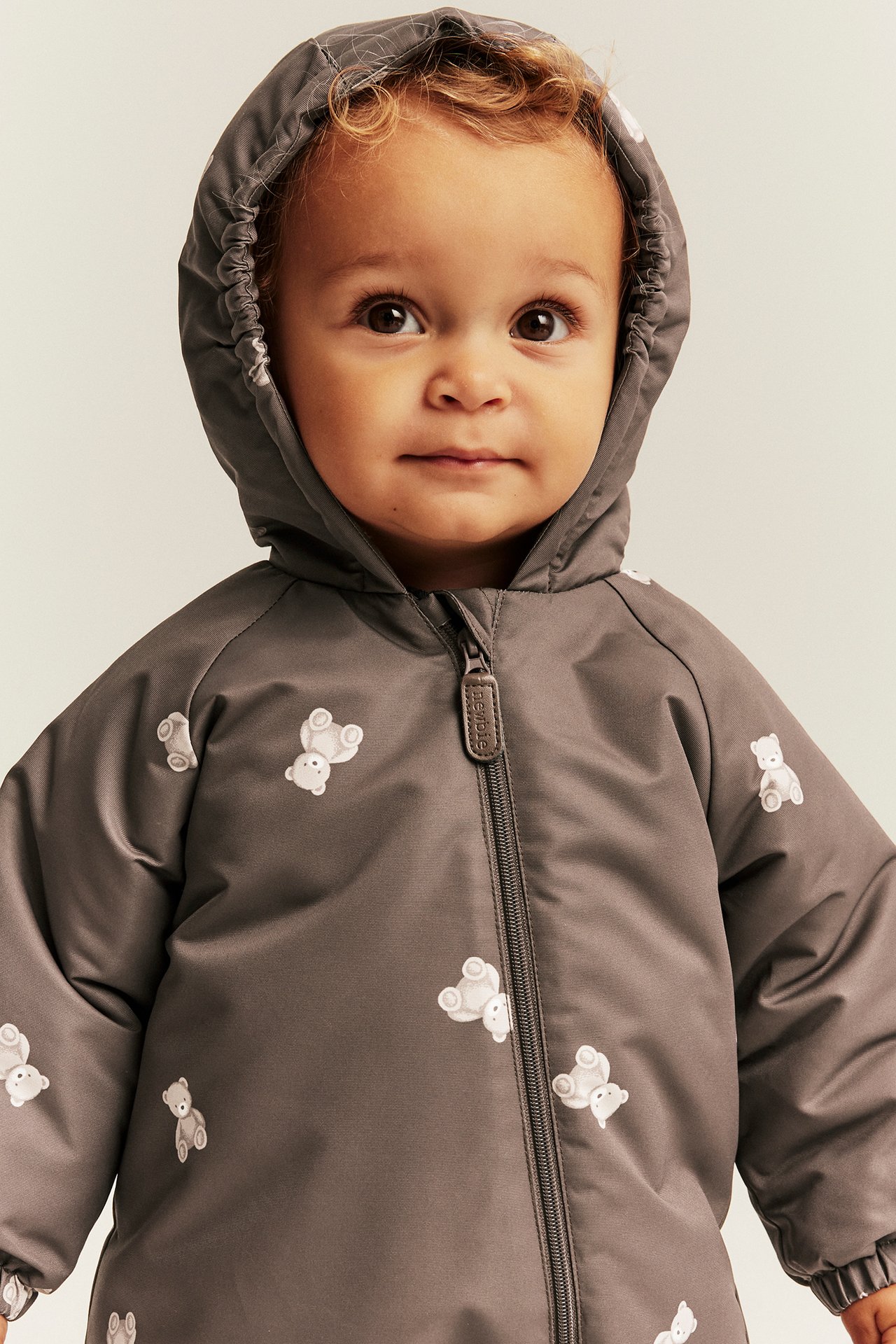 Close-up of baby in gray hooded romper with white teddy bear print, front zip.