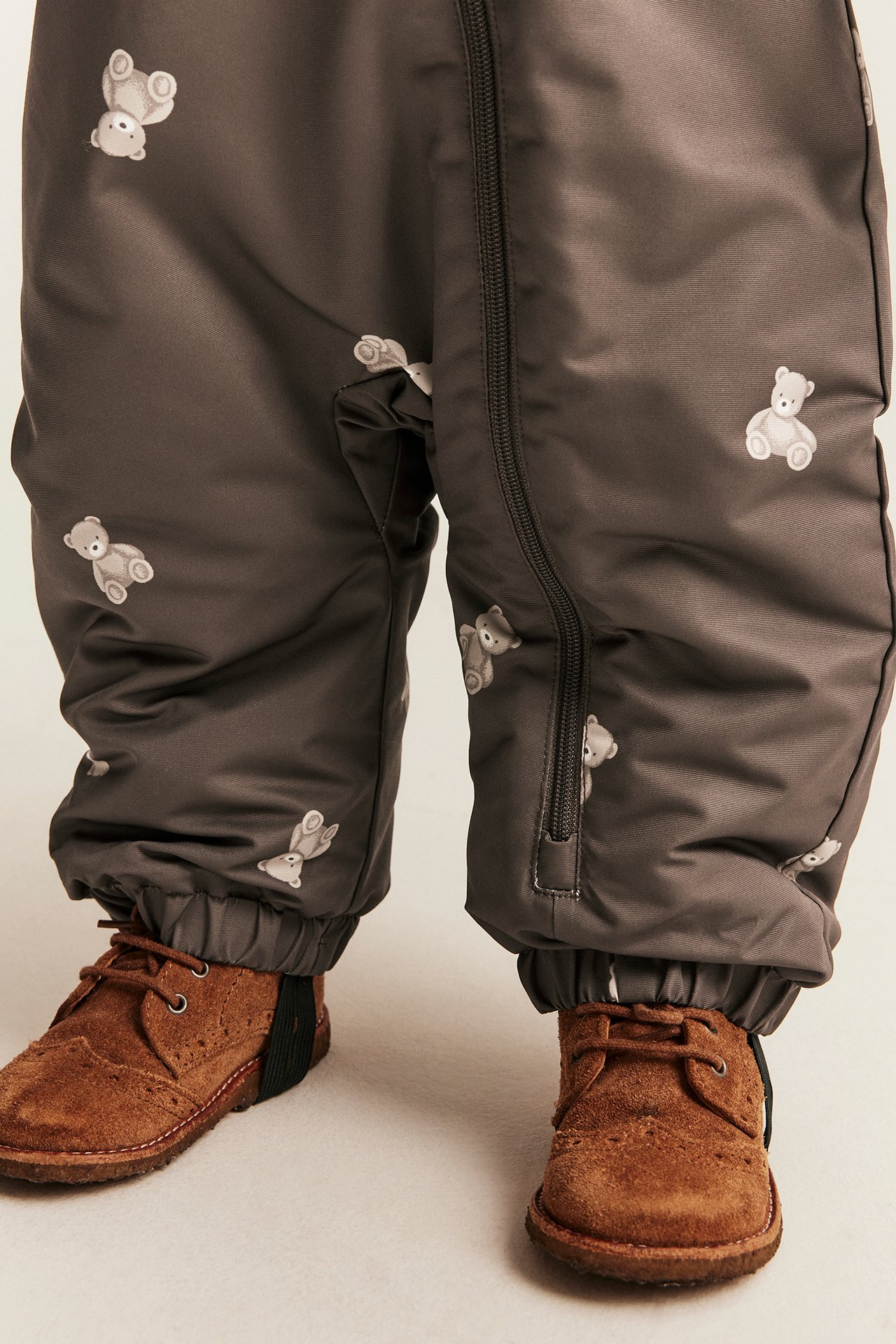 Close-up of kid's dark brown overall with teddy bear print and brown suede lace-up shoes.