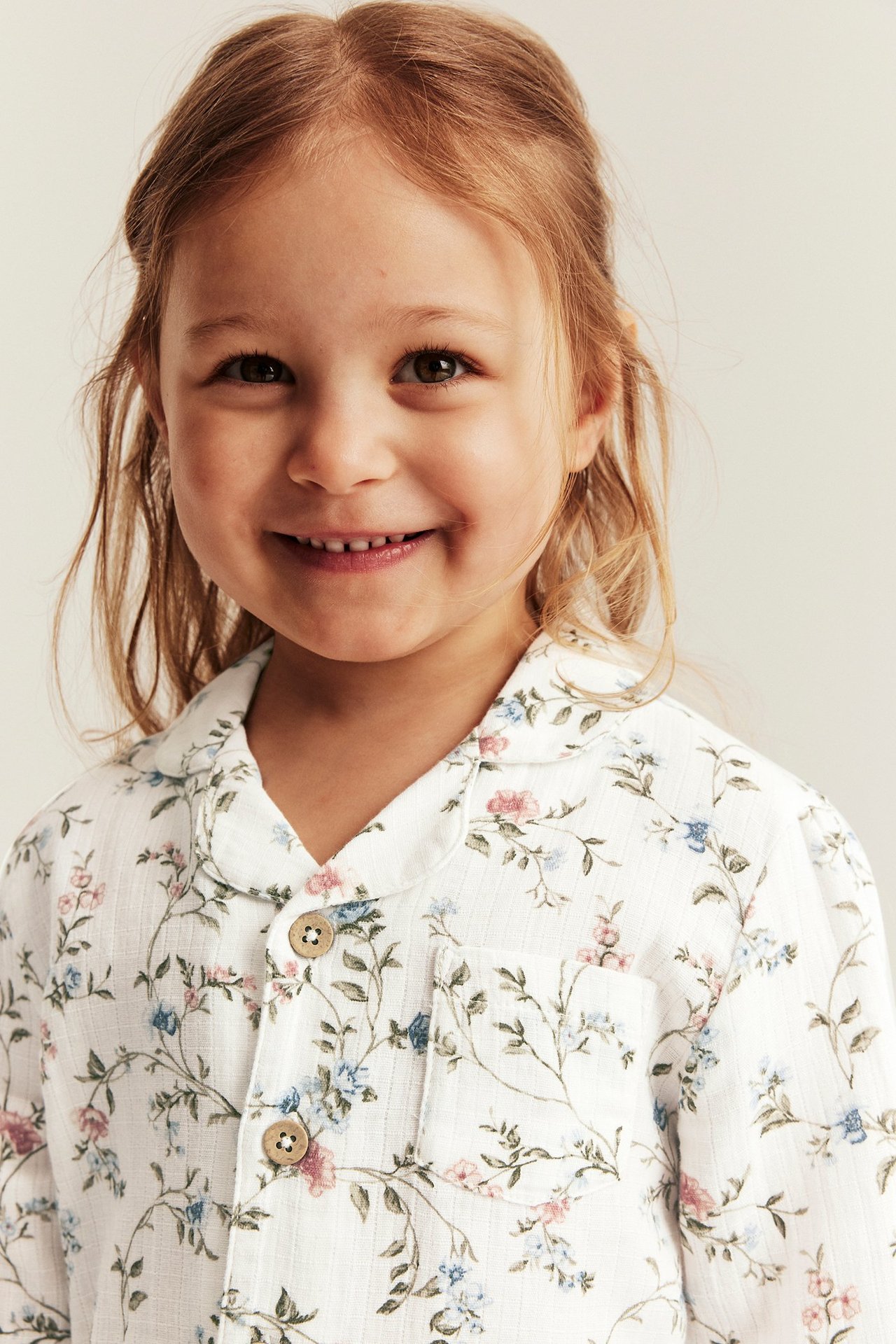 Close-up front view of a smiling kid wearing an offwhite cotton floral pajama shirt with buttons.