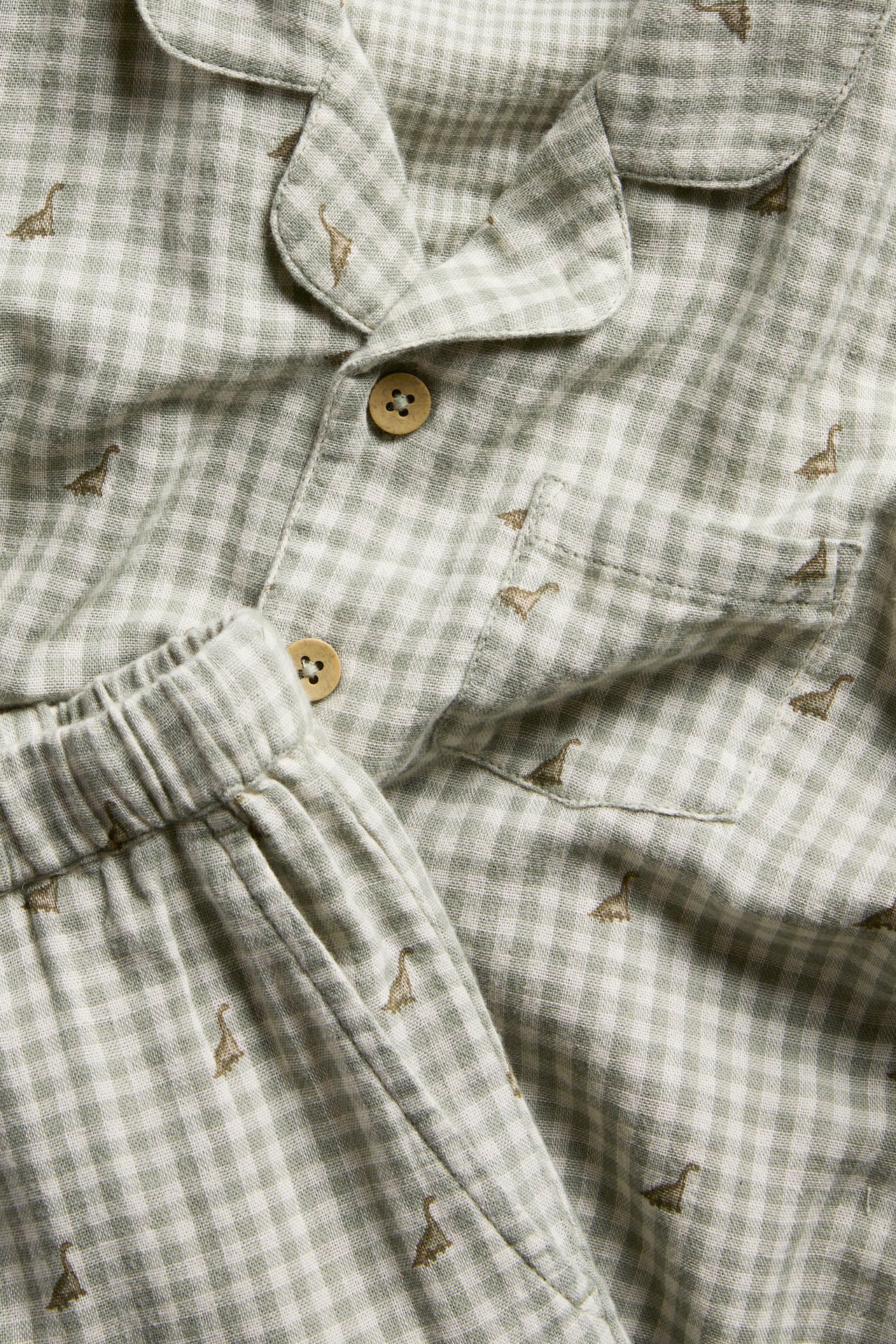 Close-up of a kid's two-piece cotton pyjamas in light green and white check with small dinosaur patterns.