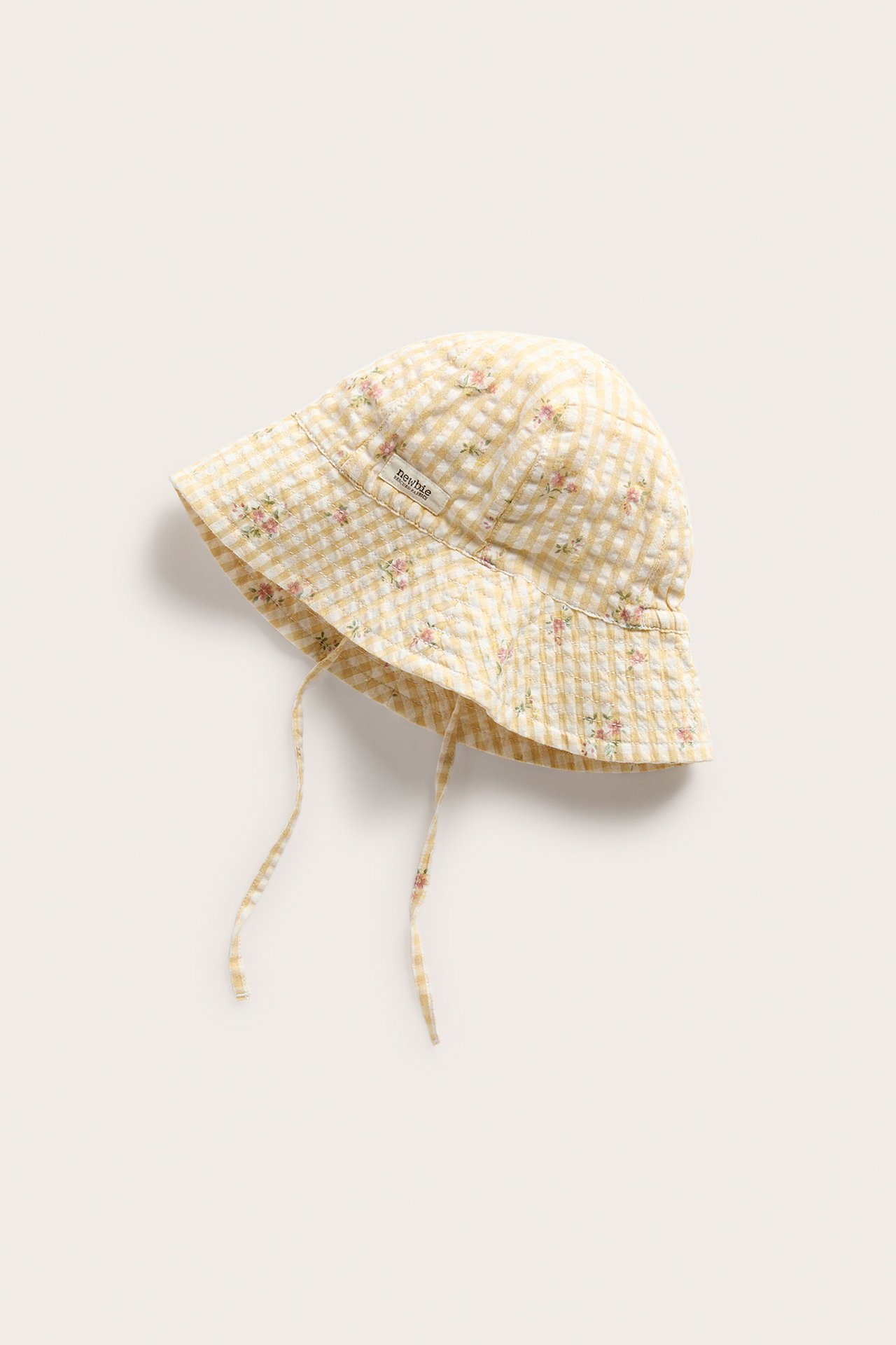 Front/side view of a yellow and white gingham woven sun hat with small floral print and tie straps.