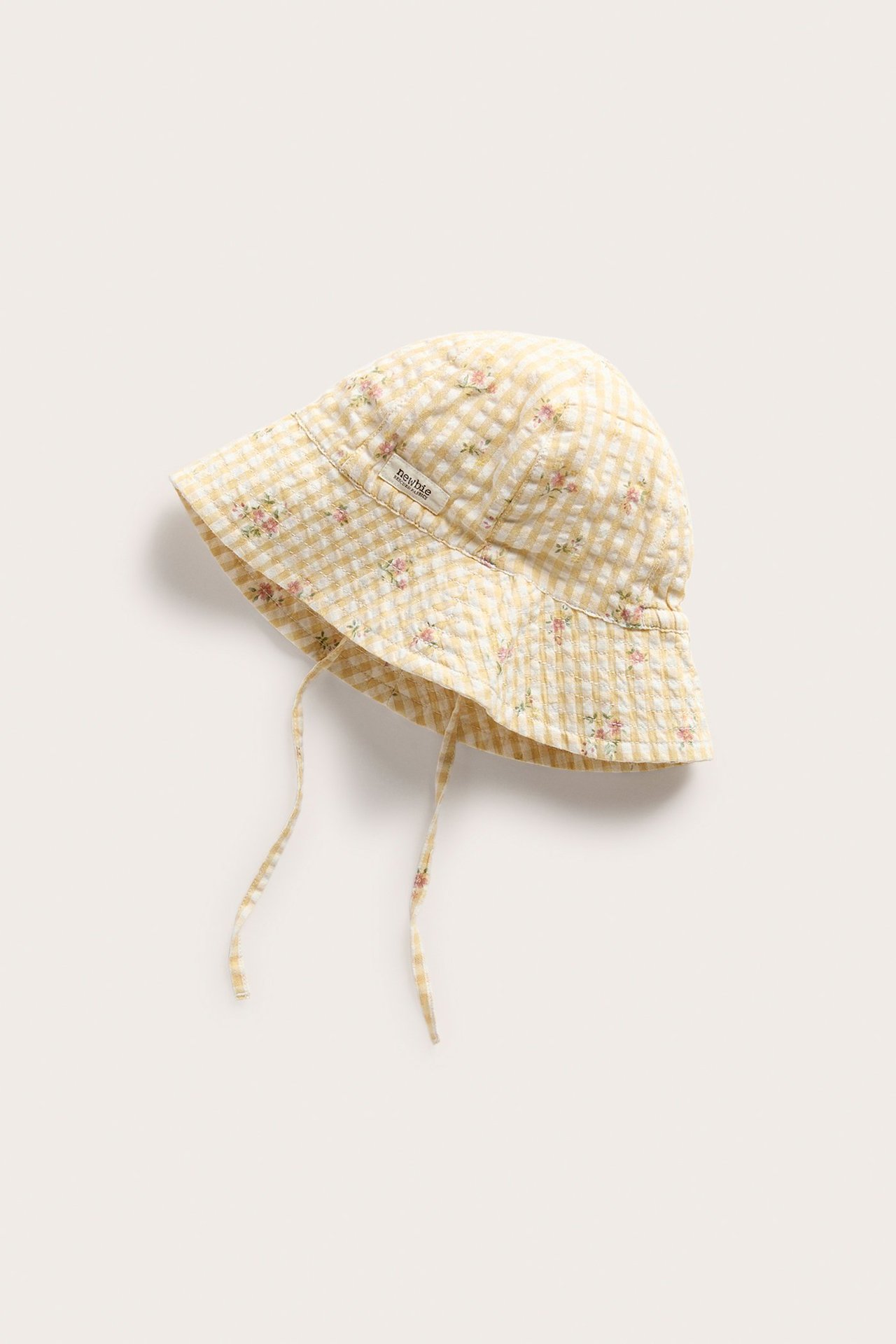 Front/side view of a yellow and white gingham woven sun hat with small floral print and tie straps.