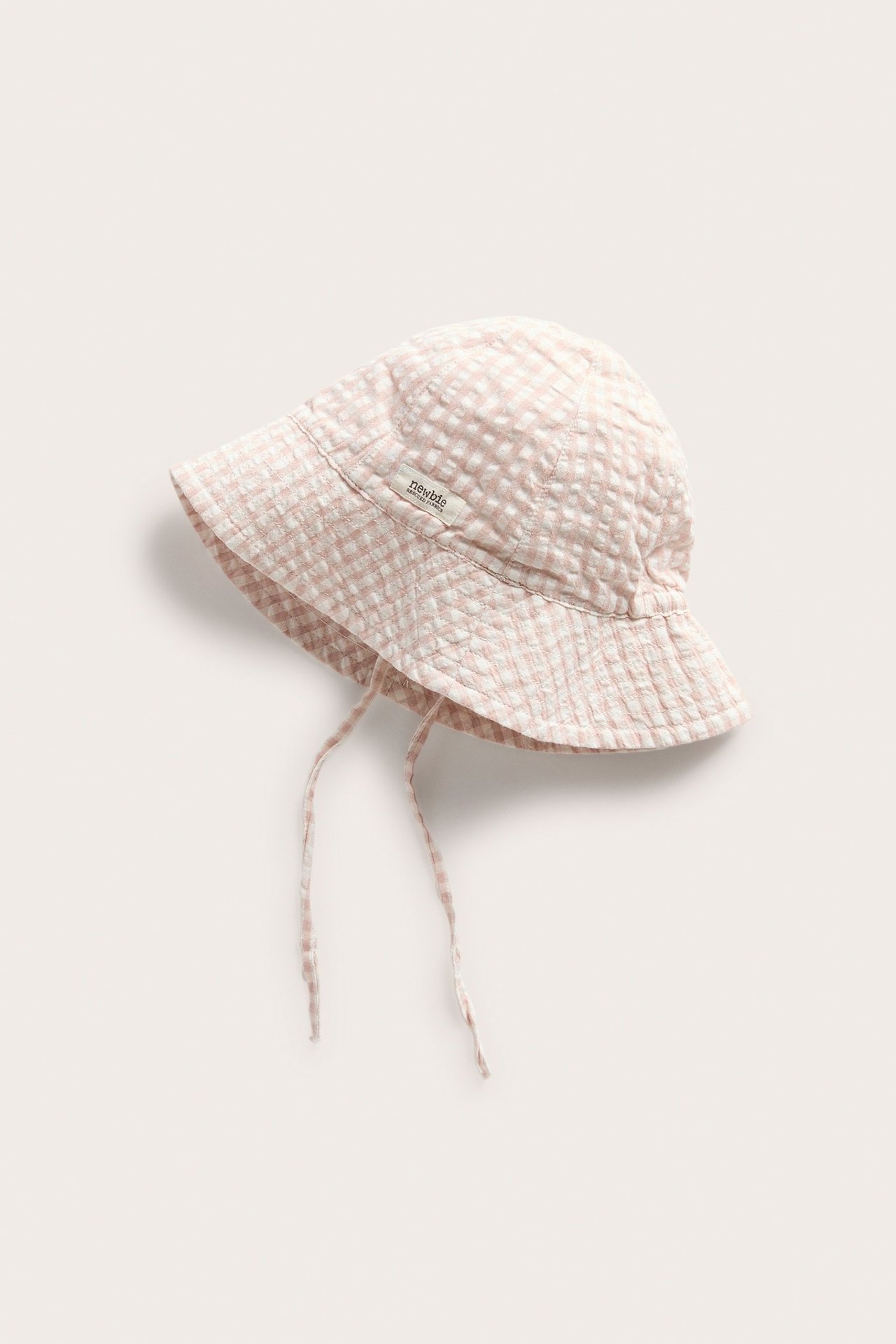 Close-up of a baby's light pink and white checked woven sun hat with tie straps.