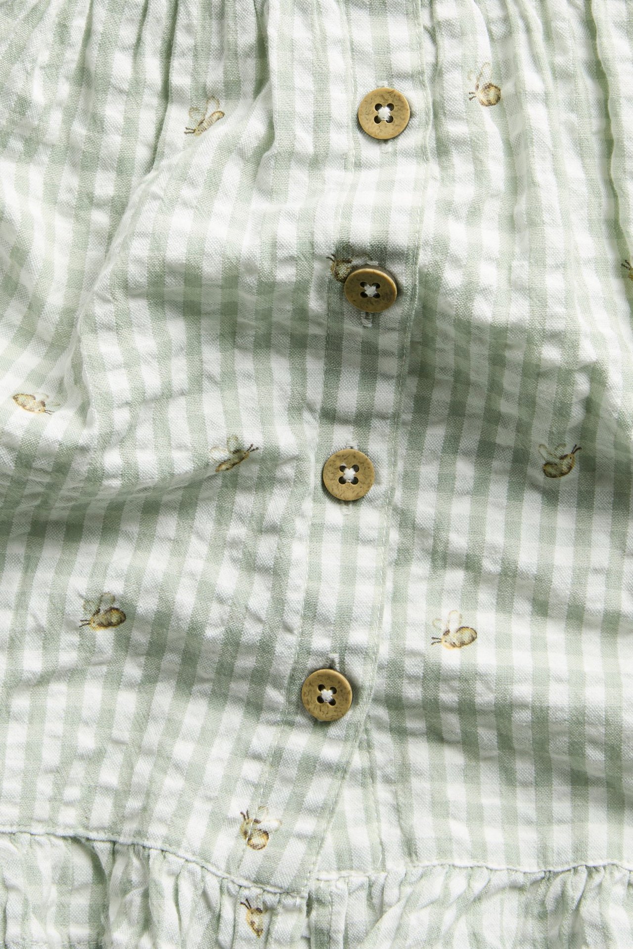 Close-up of a green and white checked cotton dress with bee embroidery, front buttons, and a ruffled hem.