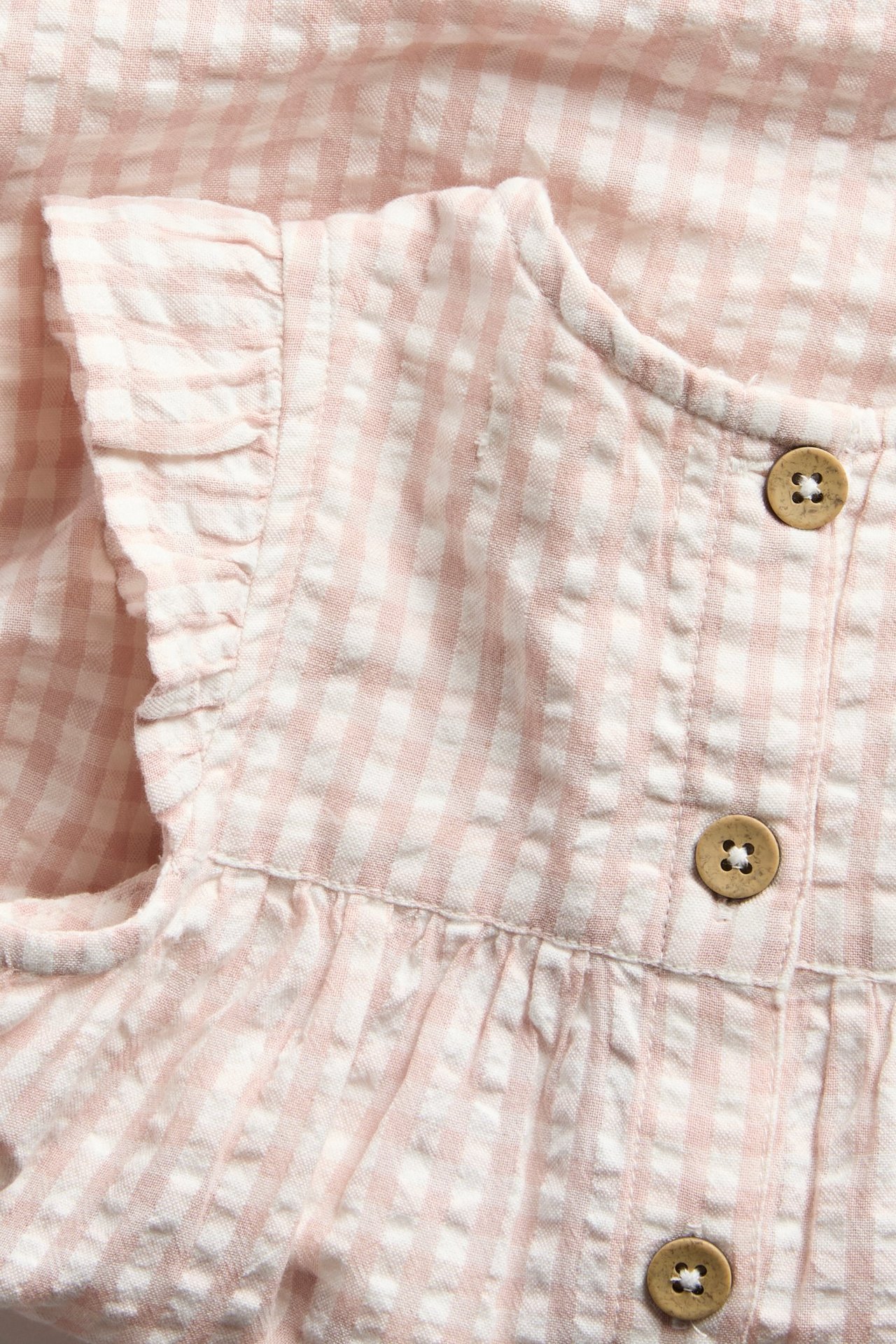 Close-up of a light pink and white checked cotton dress with ruffled sleeves and brown buttons.