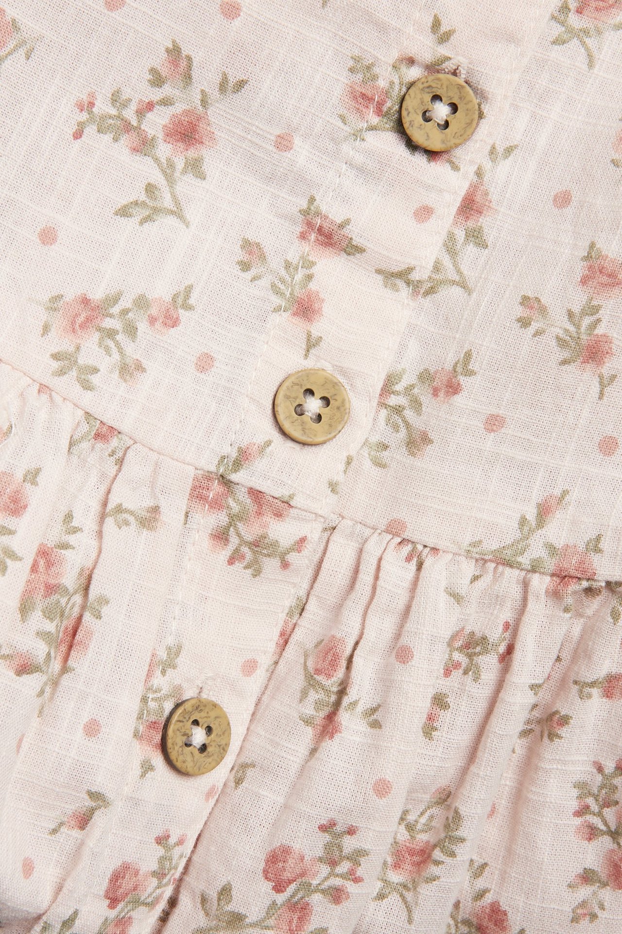 Close-up of a light pink floral dress with gathered fabric and three round wooden buttons.