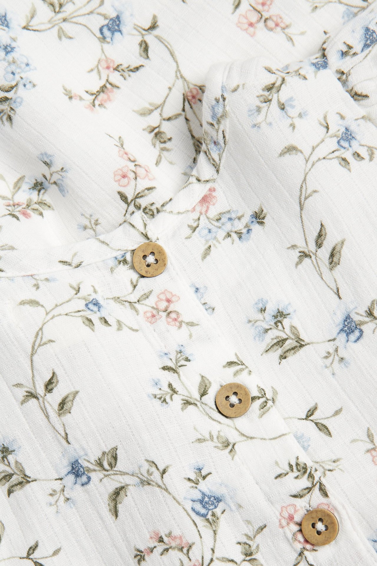 Close-up of an off-white ribbed dress with blue, pink floral pattern and brown buttons.