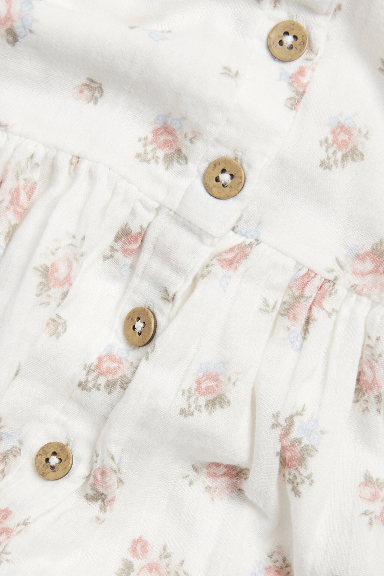Close-up of an off-white dress with a pink and blue floral pattern and wooden button fastenings.