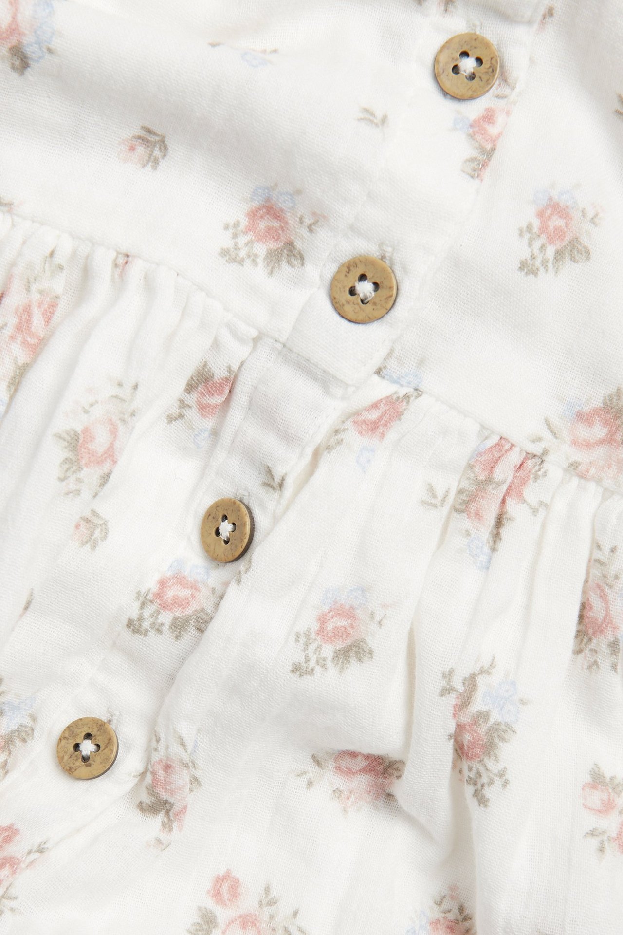 Close-up of an off-white dress with a pink and blue floral pattern and wooden button fastenings.